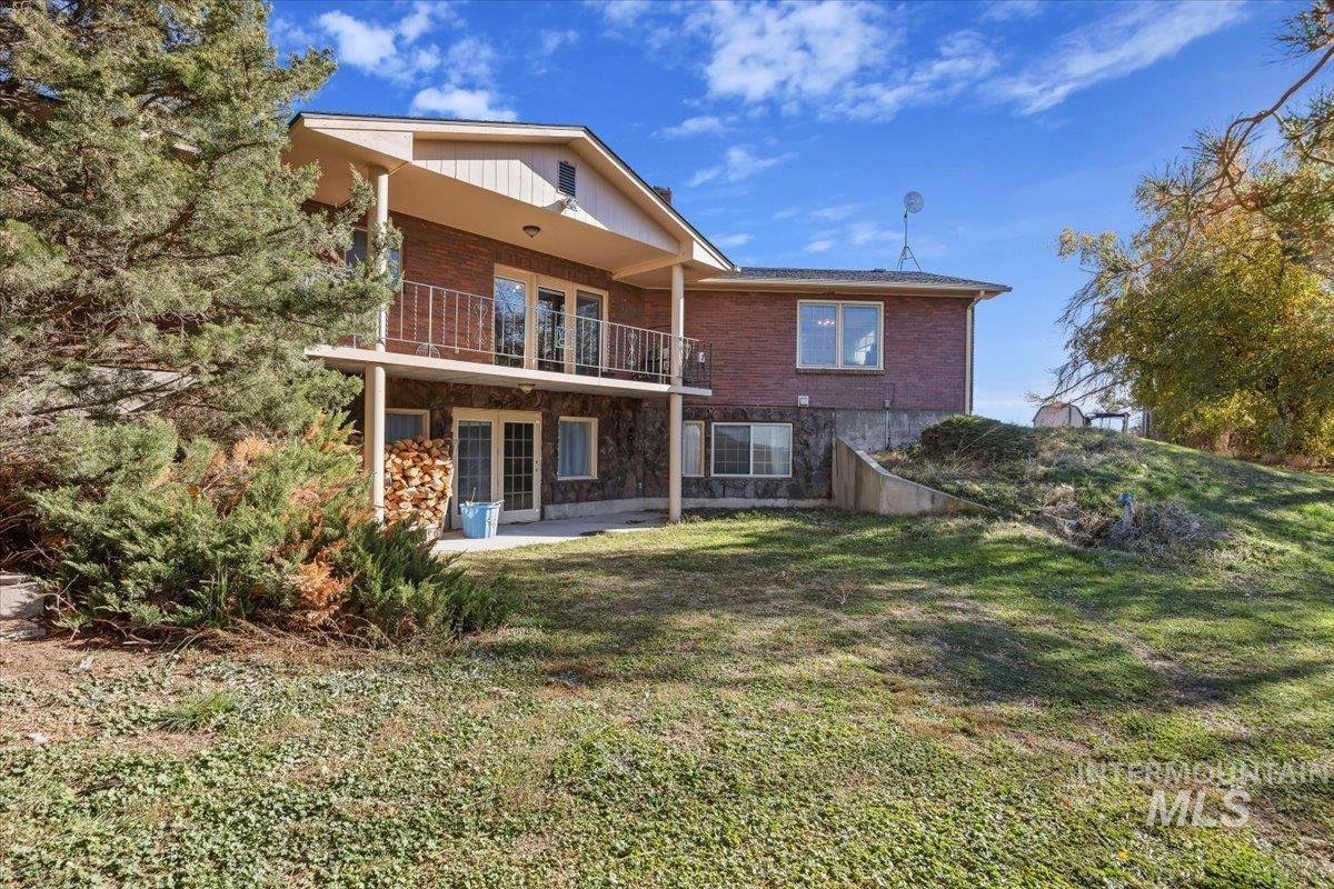 Rear view of property featuring a balcony, a patio, a yard, and brick siding