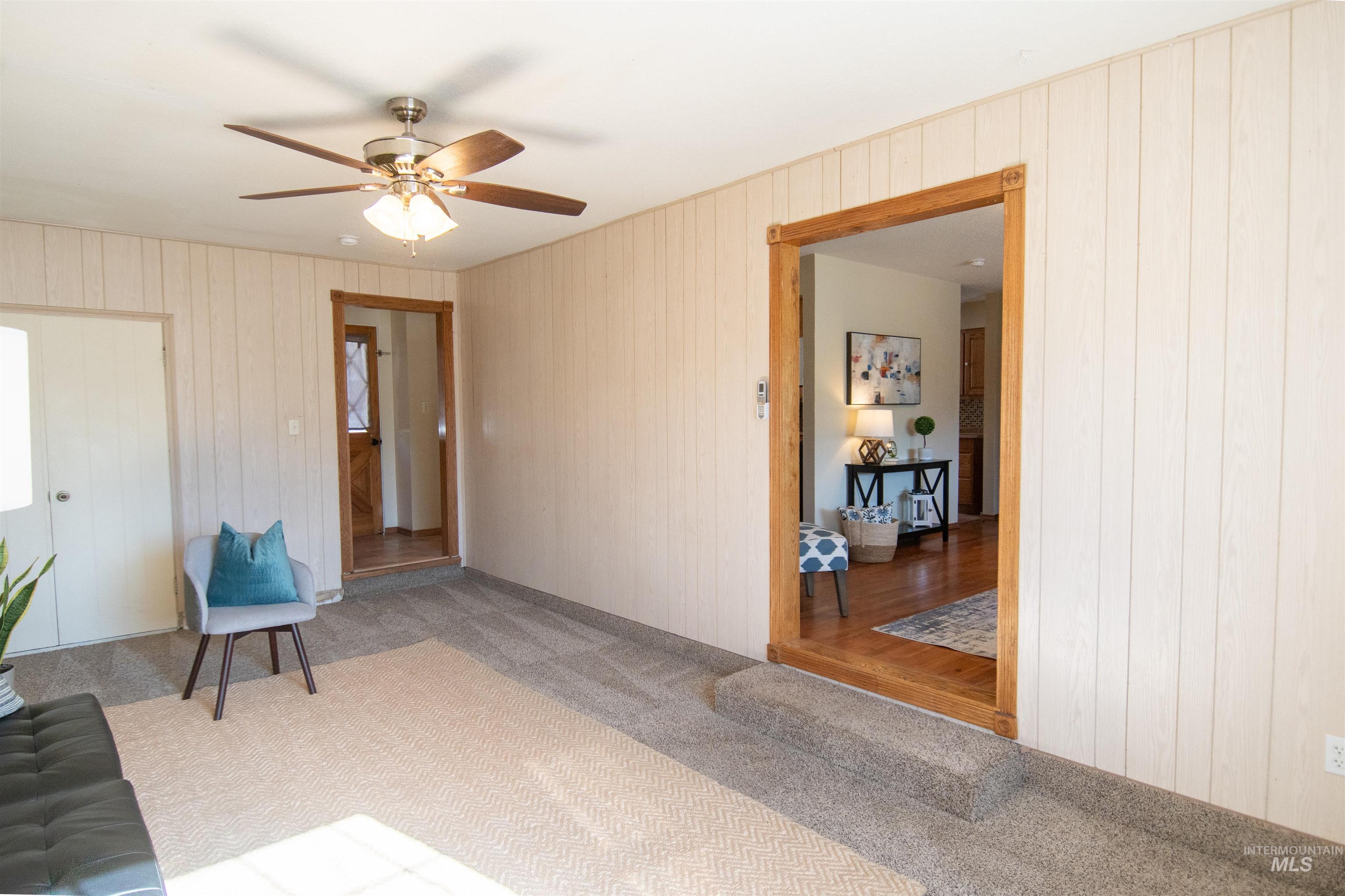 Living area featuring carpet, wood walls, and ceiling fan