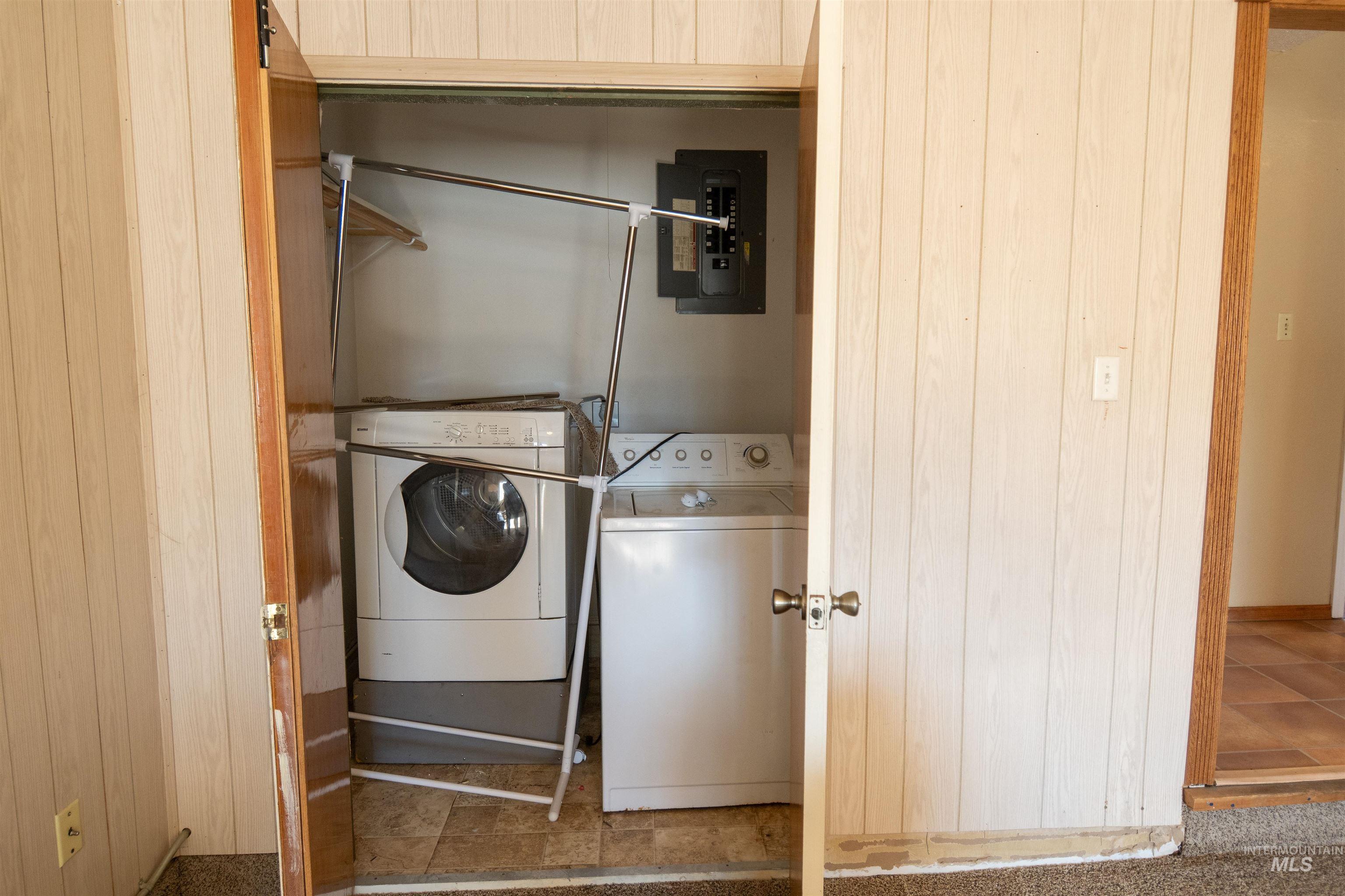 Washroom with washing machine and dryer, electric panel, and wooden walls