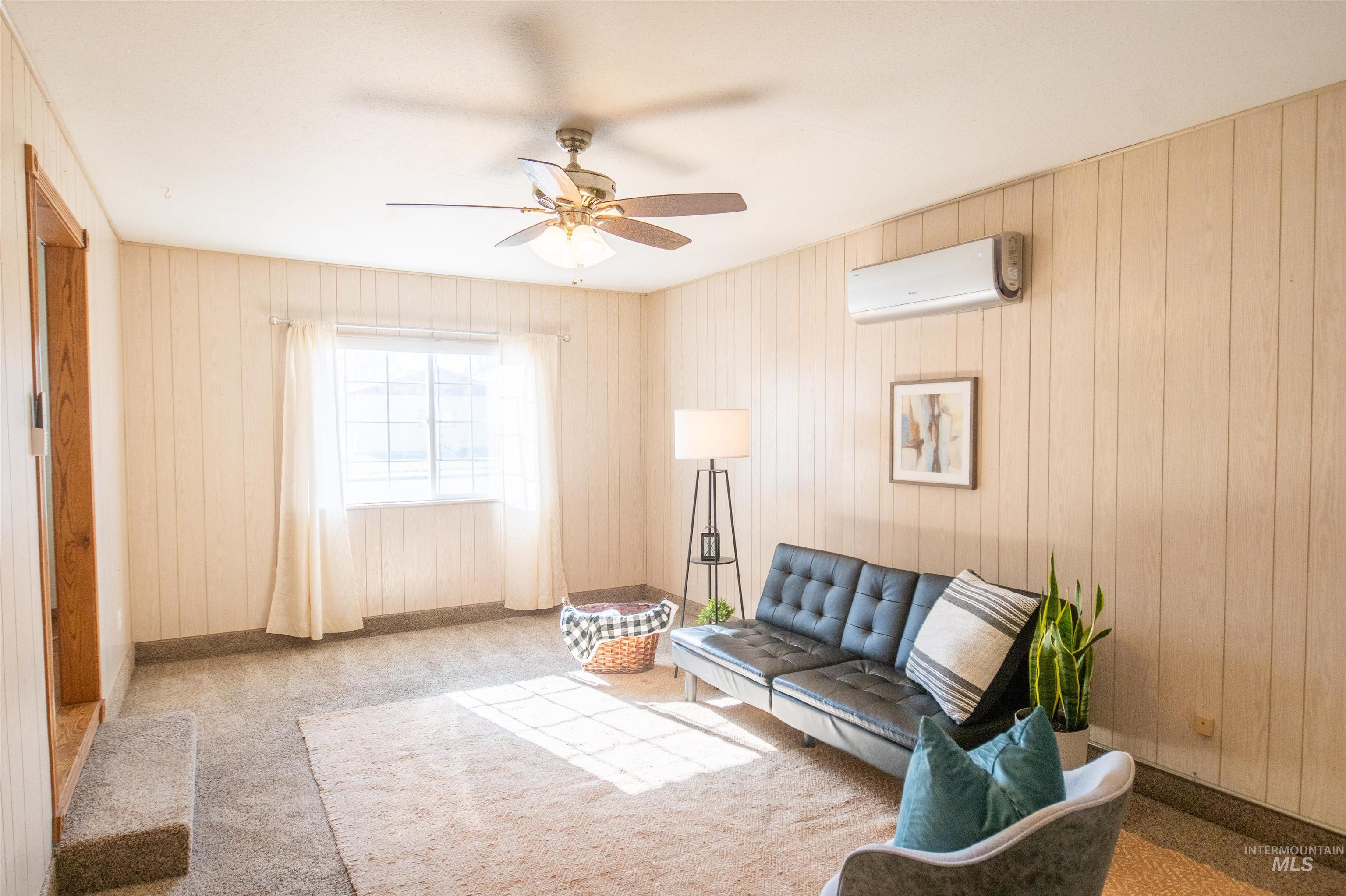 Living area with carpet flooring, a ceiling fan, and a wall mounted AC