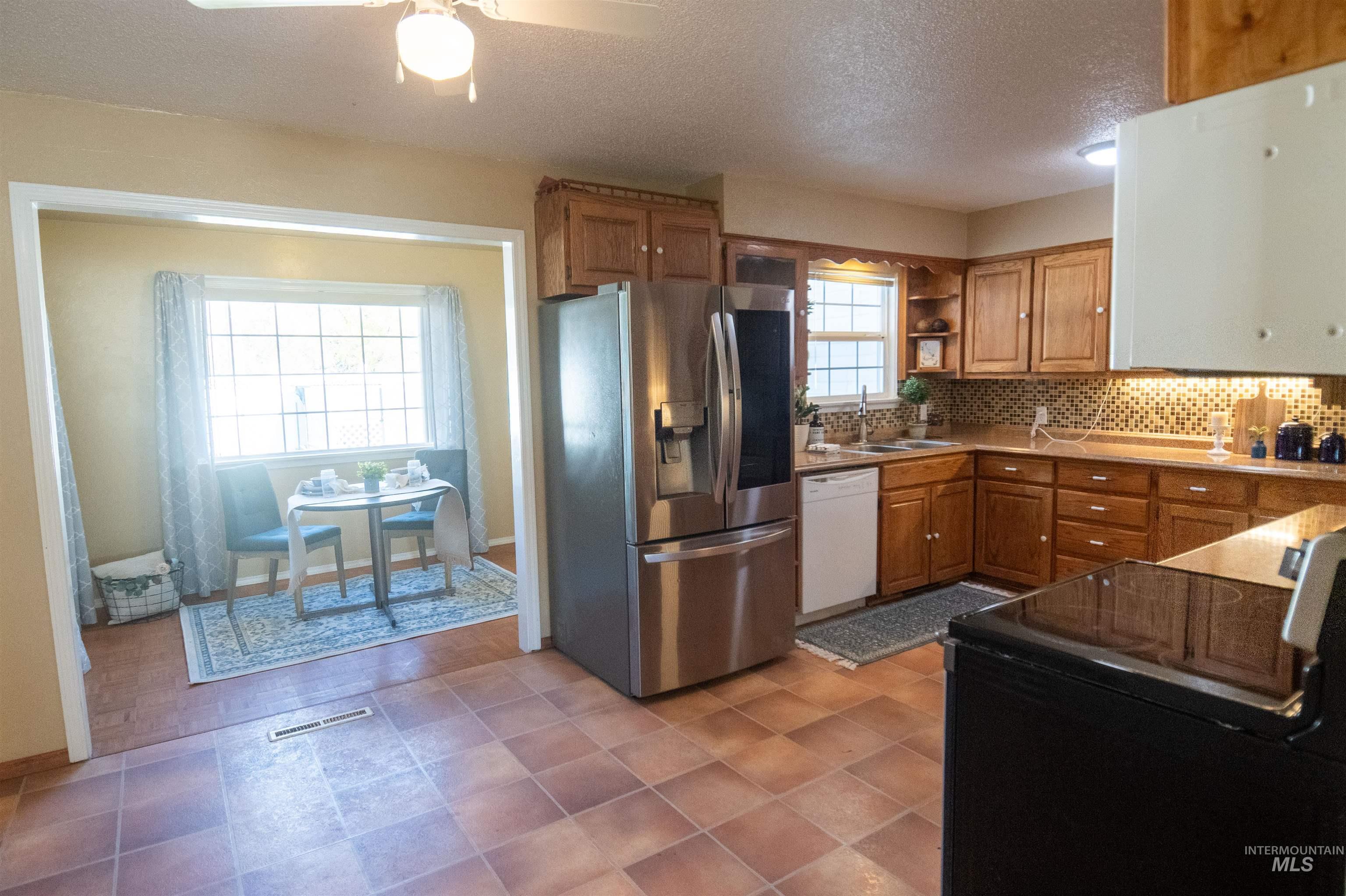 Kitchen featuring brown cabinetry, stainless steel fridge with ice dispenser, black range with electric stovetop, tasteful backsplash, and a textured ceiling