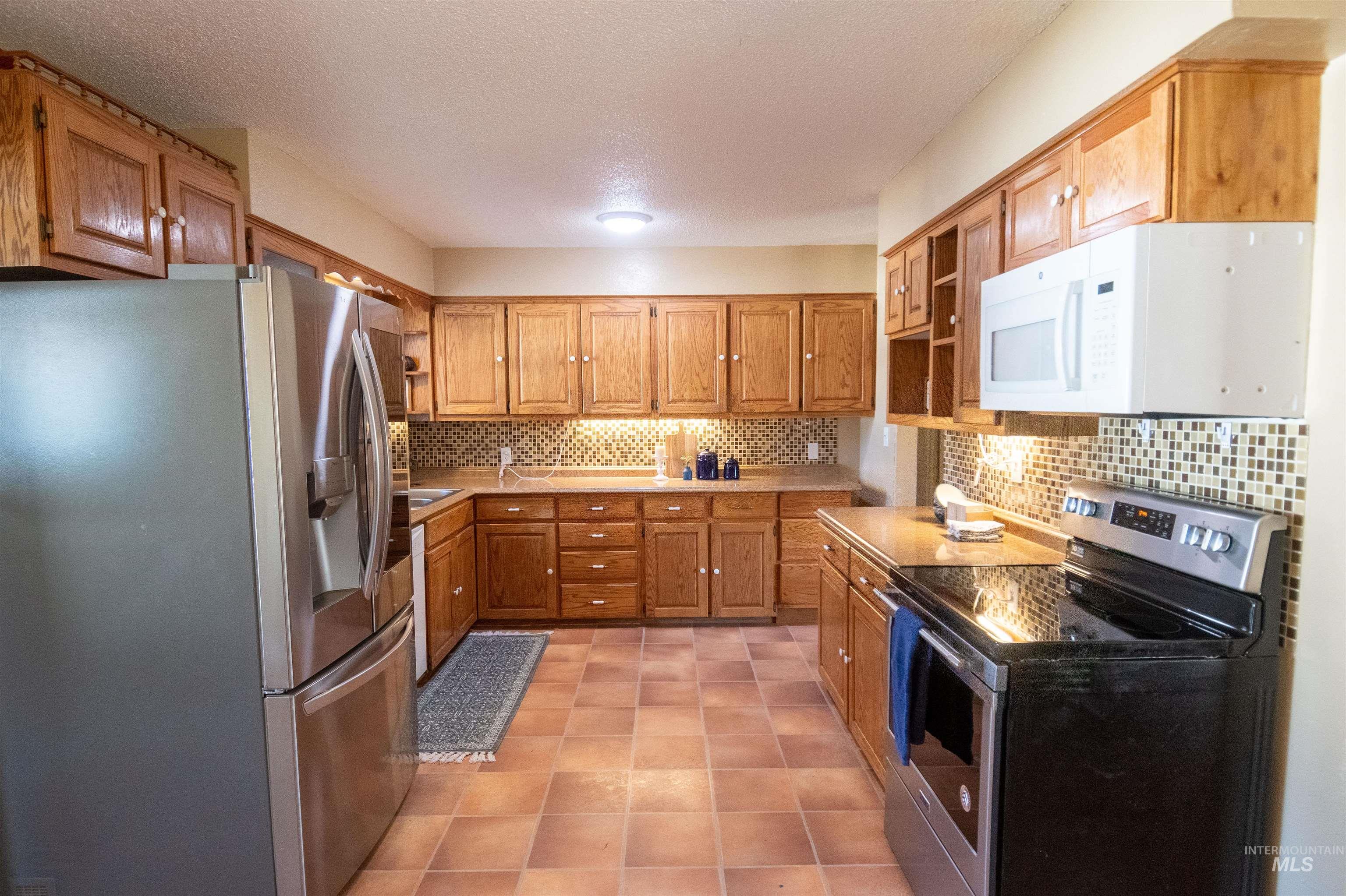 Kitchen featuring appliances with stainless steel finishes, tasteful backsplash, light countertops, brown cabinetry, and a textured ceiling