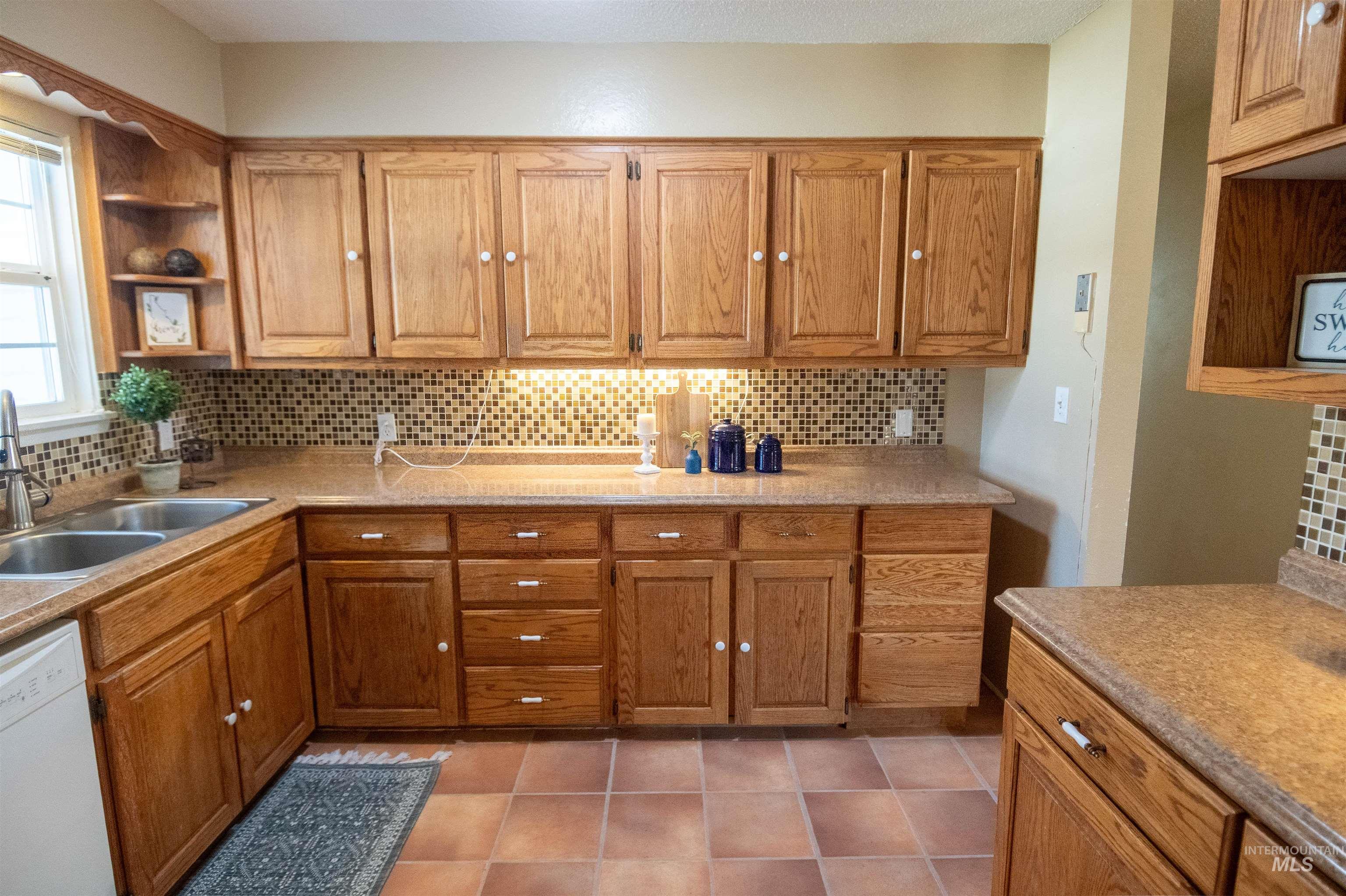 Kitchen featuring open shelves, brown cabinets, decorative backsplash, and dishwasher