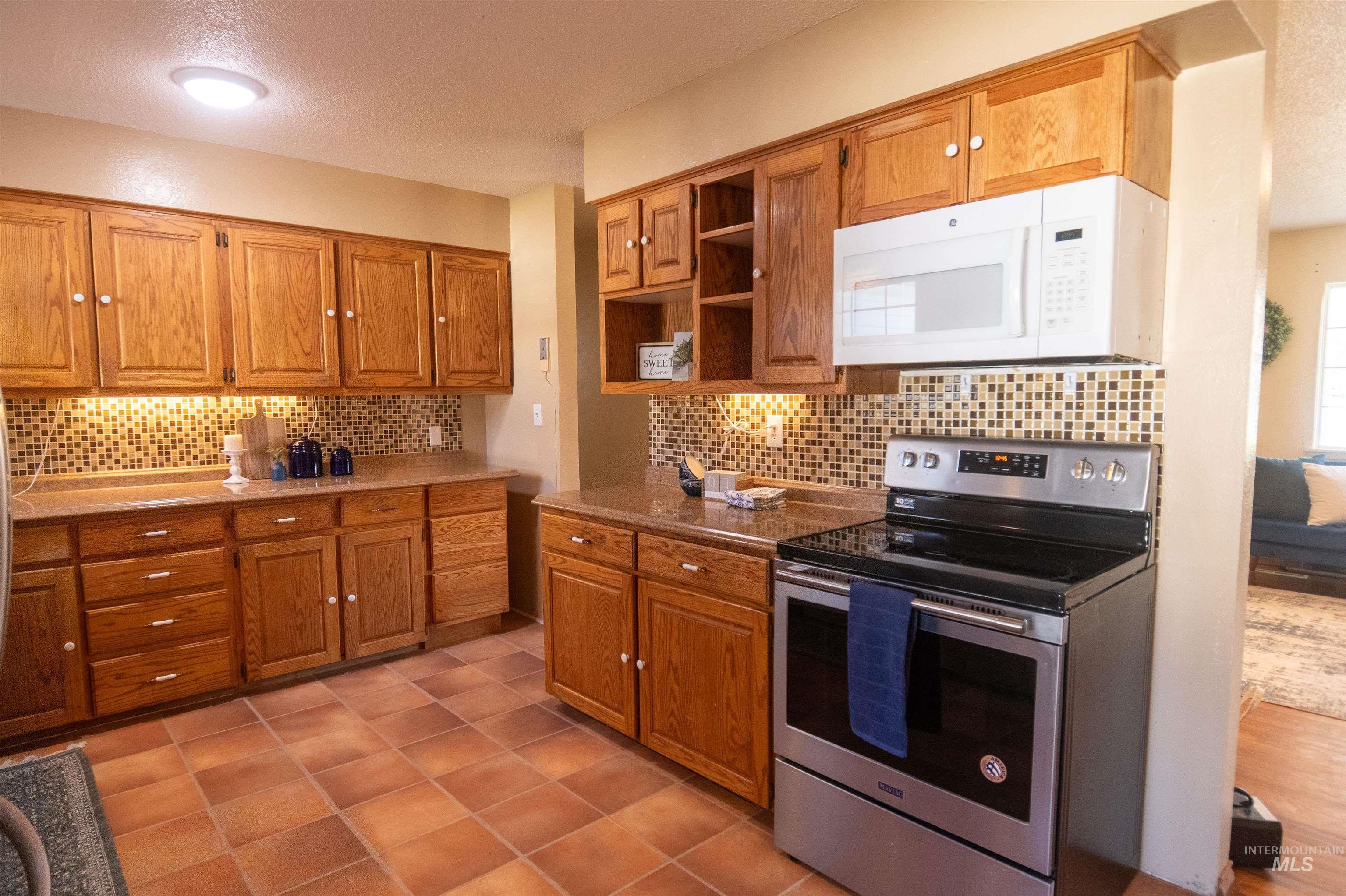 Kitchen featuring stainless steel electric range, white microwave, a textured ceiling, open shelves, and decorative backsplash