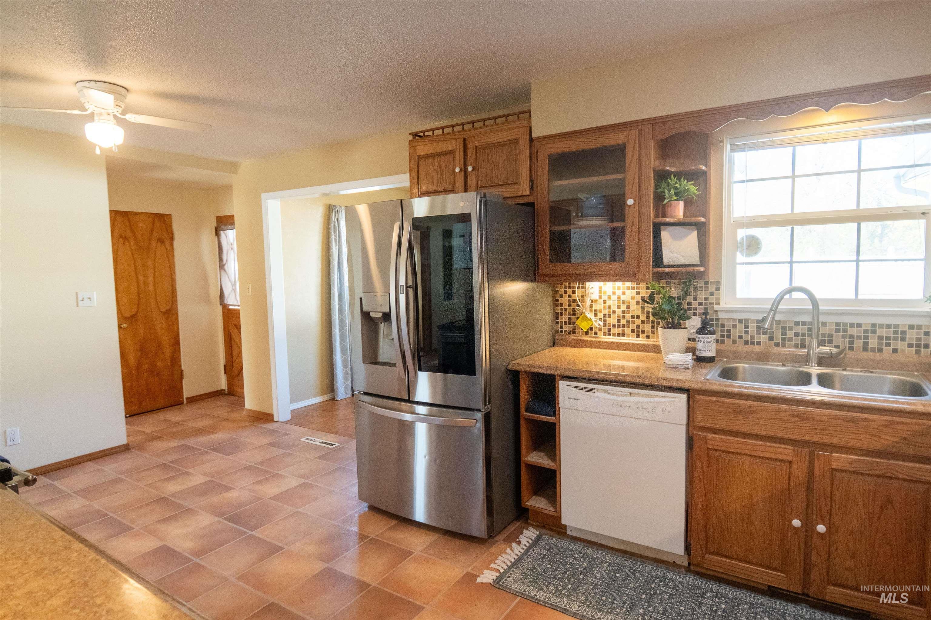 Kitchen featuring brown cabinets, open shelves, decorative backsplash, white dishwasher, and stainless steel fridge with ice dispenser