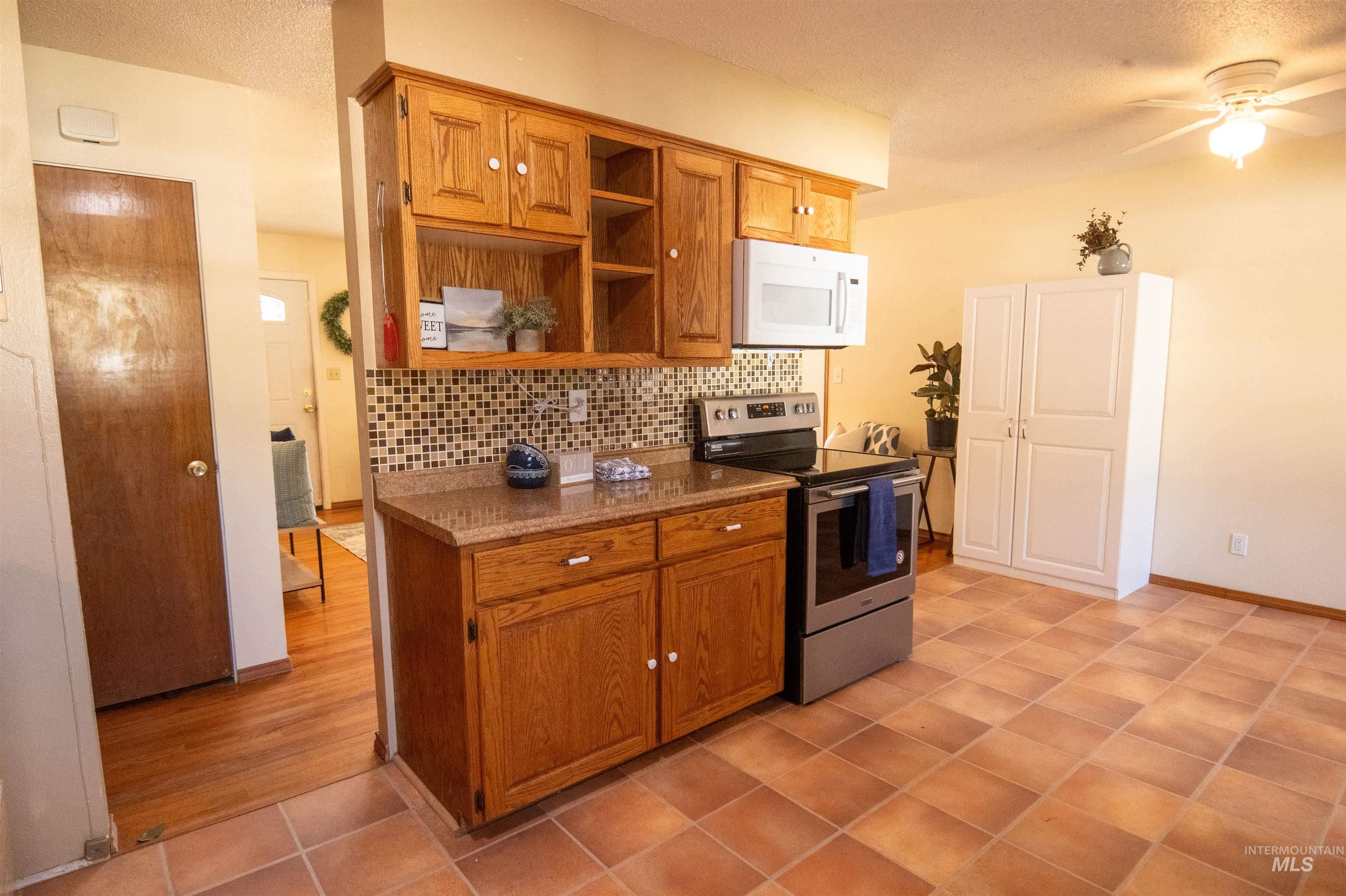 Kitchen featuring brown cabinetry, stainless steel electric stove, tasteful backsplash, white microwave, and a ceiling fan