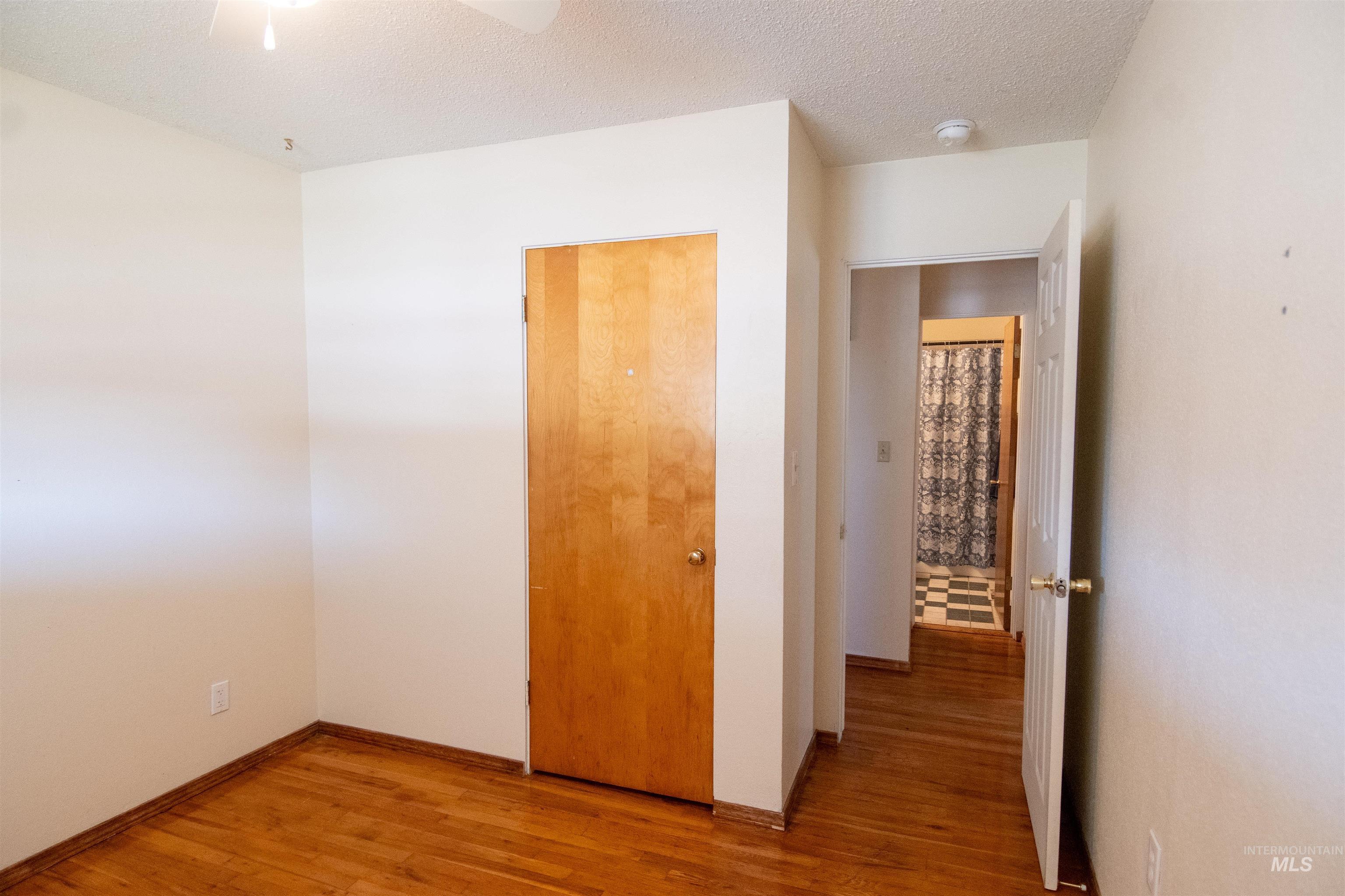 Unfurnished bedroom with wood finished floors, a textured ceiling, a closet, and ceiling fan