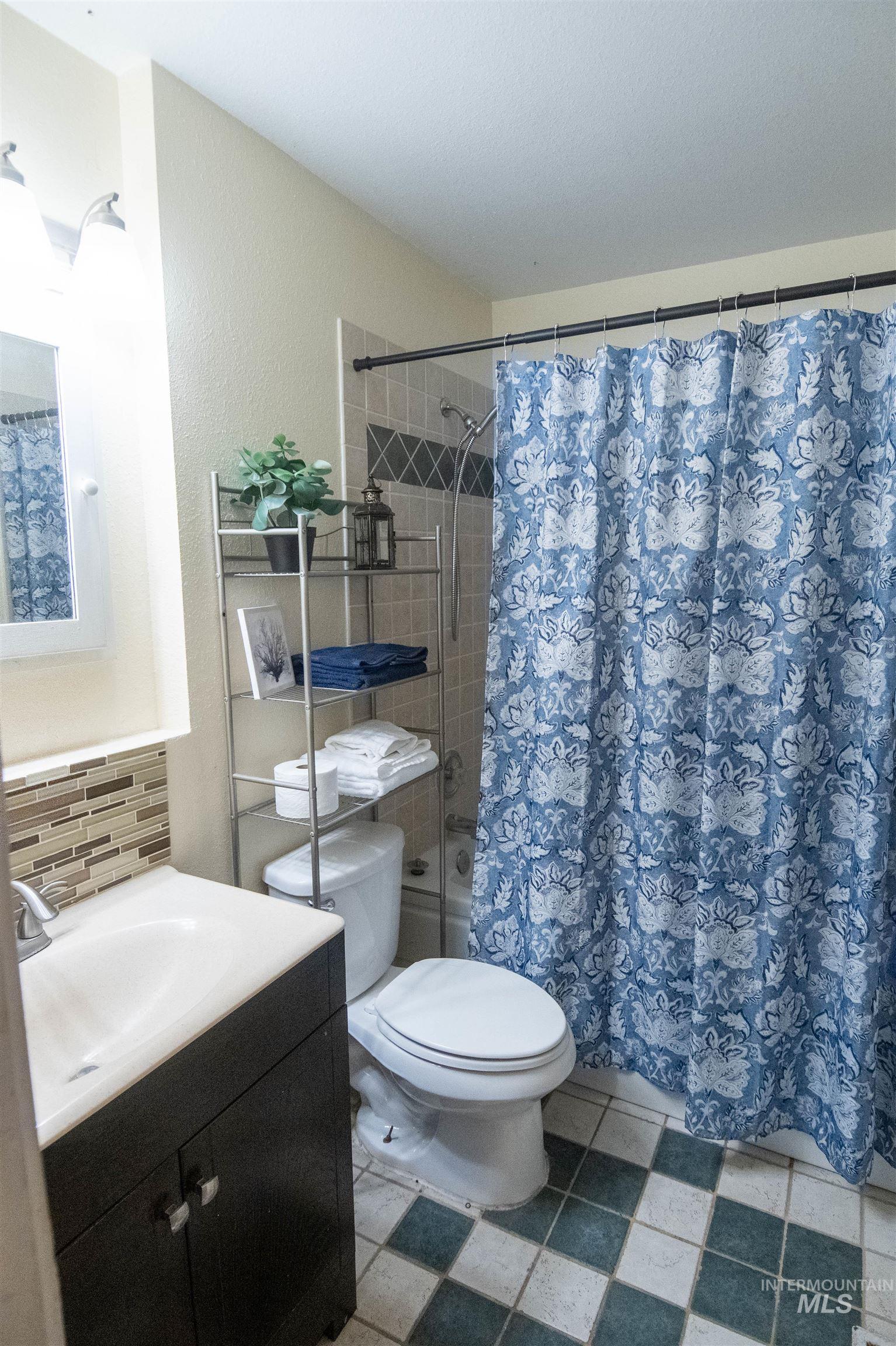Full bathroom featuring vanity, shower / bath combination with curtain, backsplash, and tile patterned flooring
