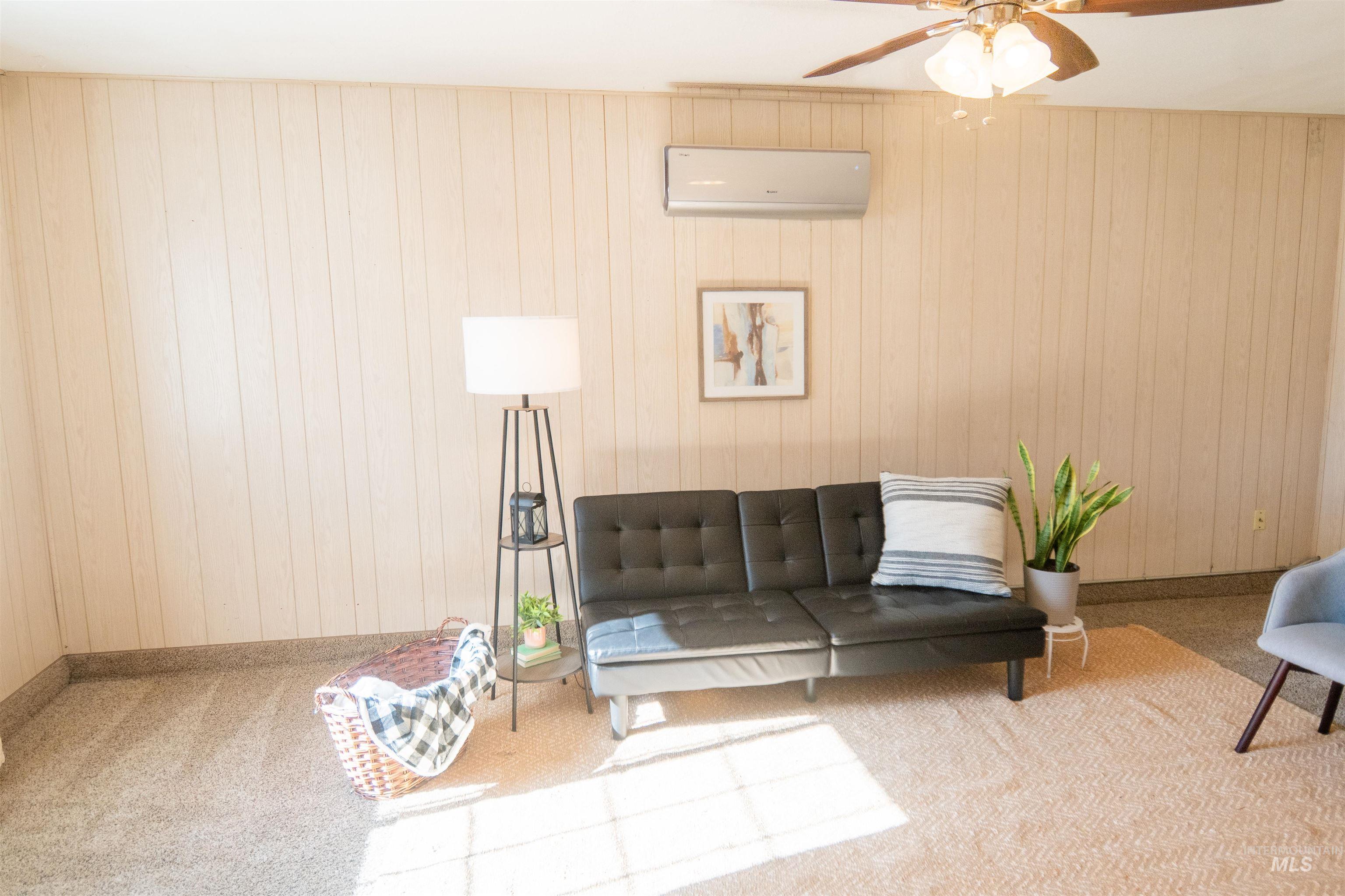 Carpeted living area with wooden walls, a wall unit AC, and a ceiling fan