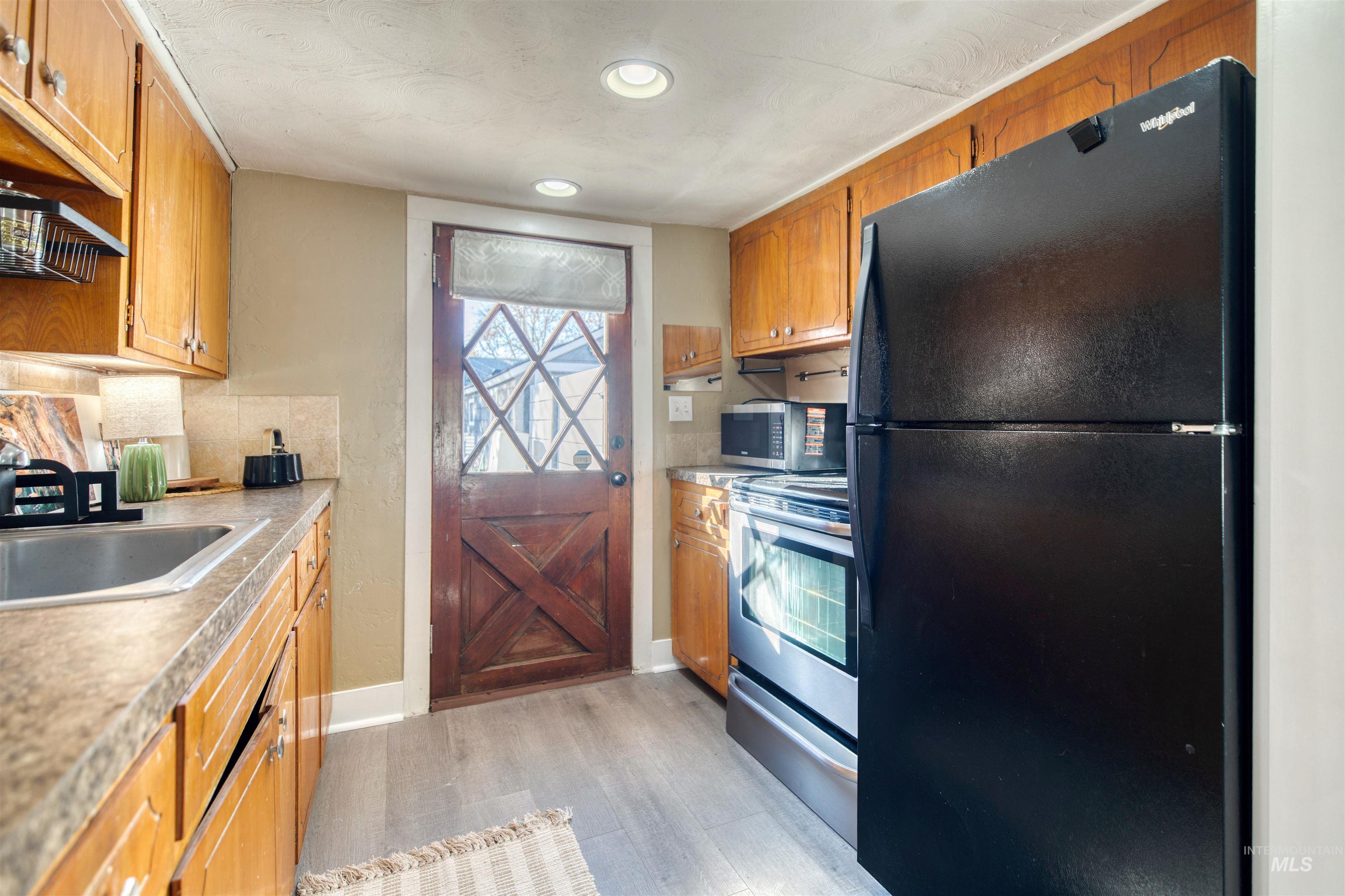 Kitchen with appliances with stainless steel finishes, light wood-style flooring, decorative backsplash, light countertops, and brown cabinets