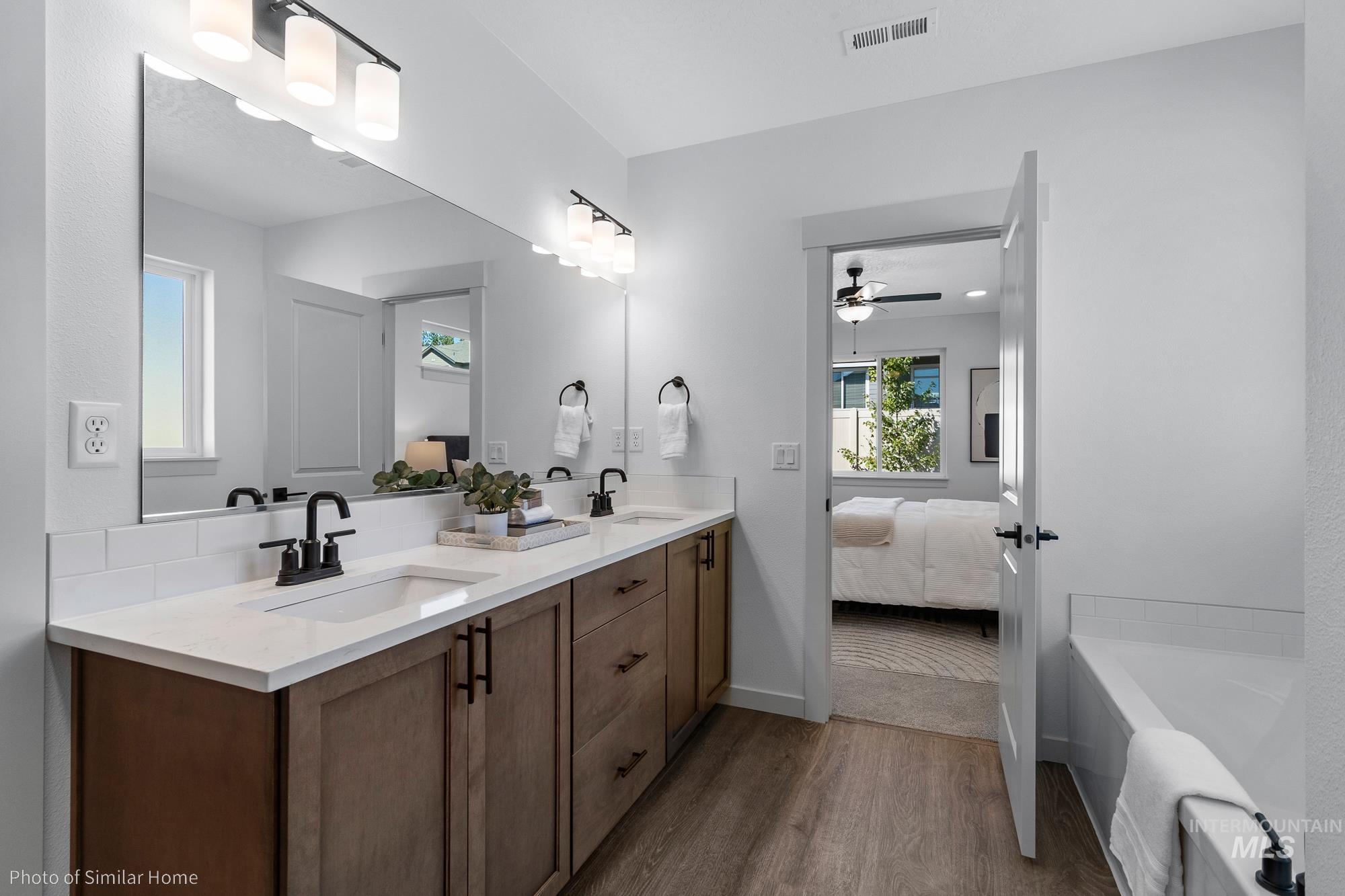 Full bathroom with dark wood-type flooring, double vanity, a bathtub, ensuite bath, and ceiling fan