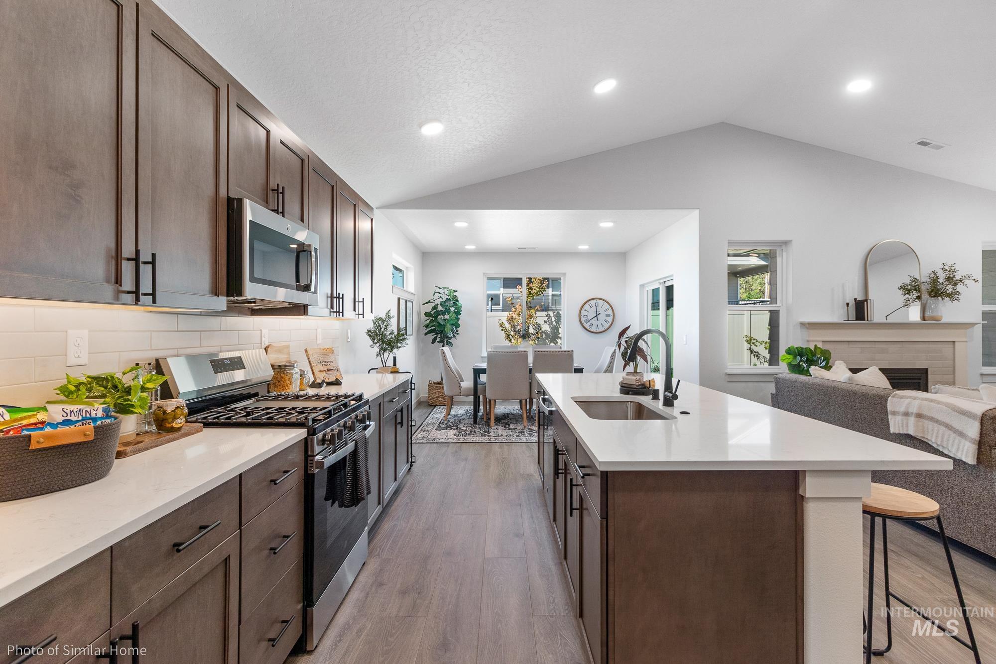 Kitchen featuring dark brown cabinets, stainless steel appliances, open floor plan, vaulted ceiling, and light wood finished floors