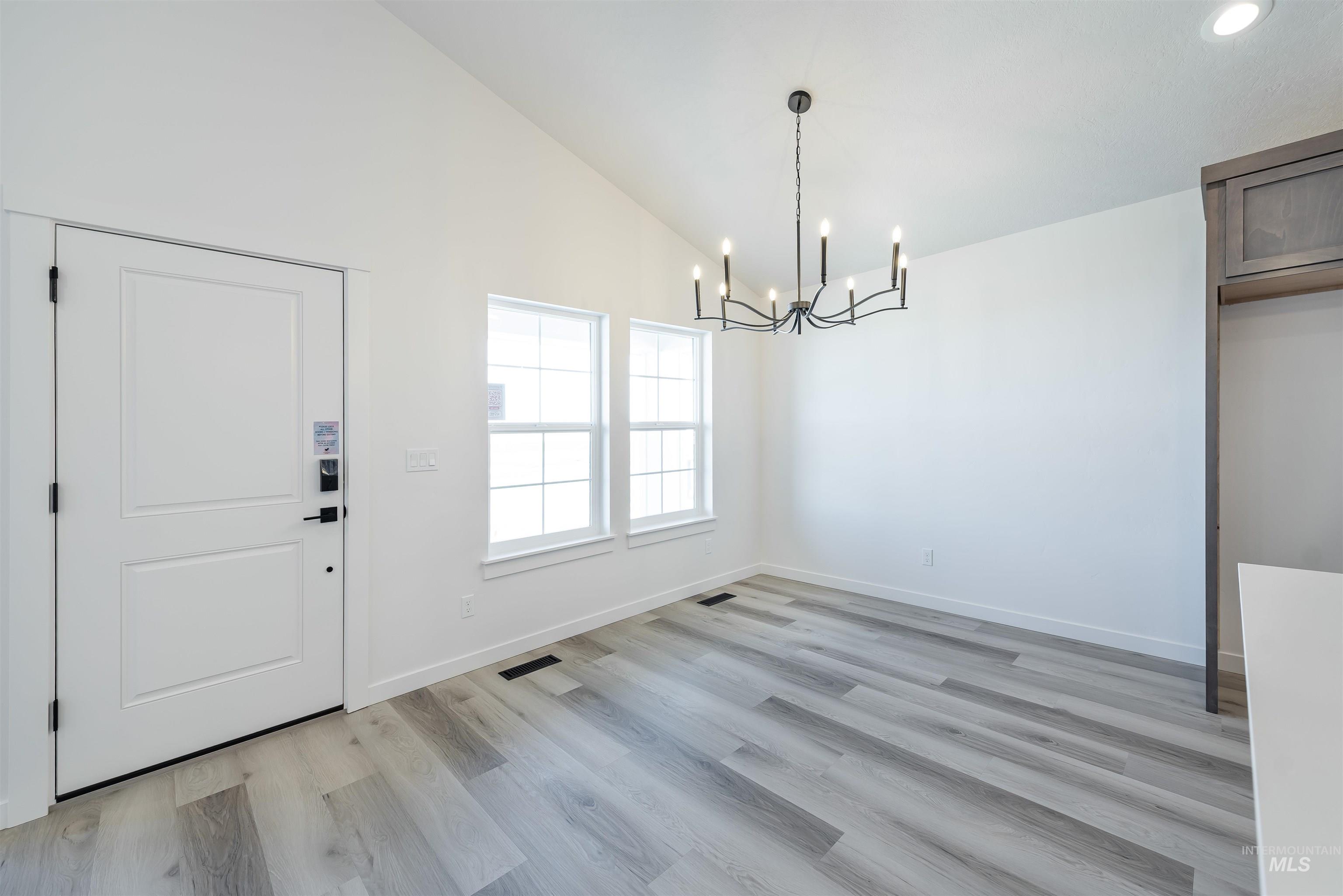 Unfurnished dining area featuring light wood finished floors, a chandelier, and high vaulted ceiling