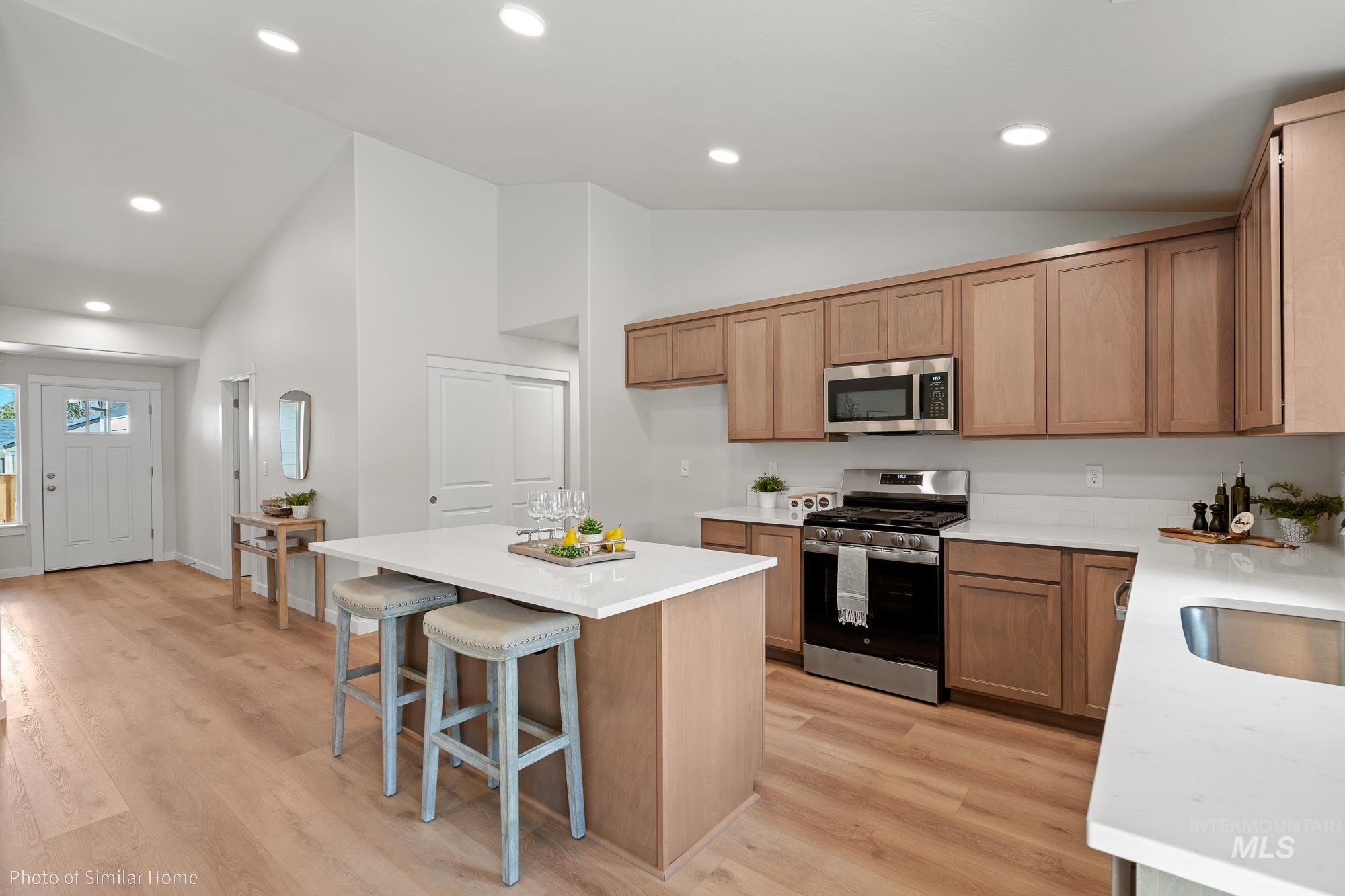 Kitchen with stainless steel appliances, light wood-style flooring, a kitchen island, light stone counters, and recessed lighting