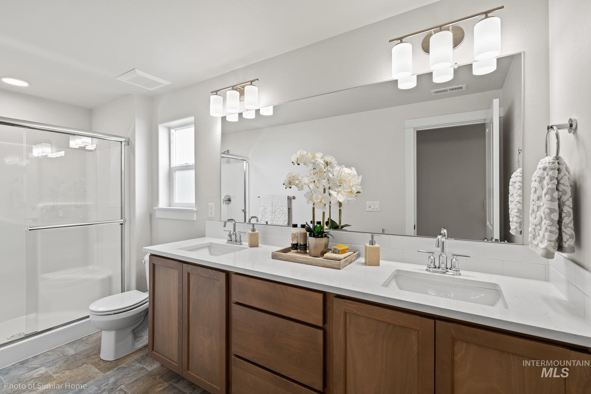 Bathroom featuring a stall shower, double vanity, and dark stone finish floors