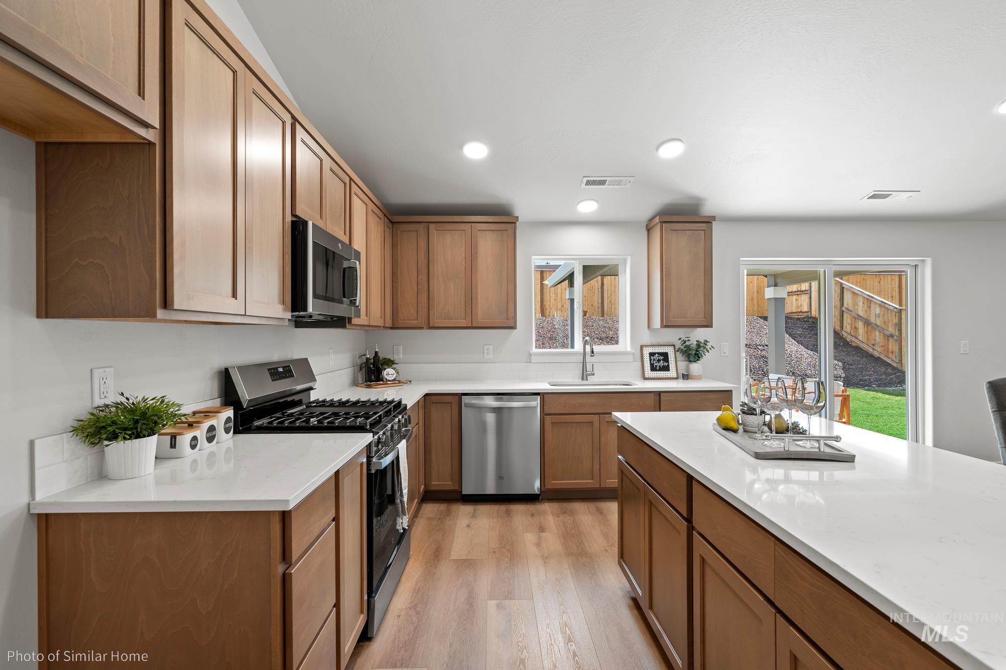 Kitchen featuring appliances with stainless steel finishes, light wood-style floors, recessed lighting, brown cabinets, and light stone counters