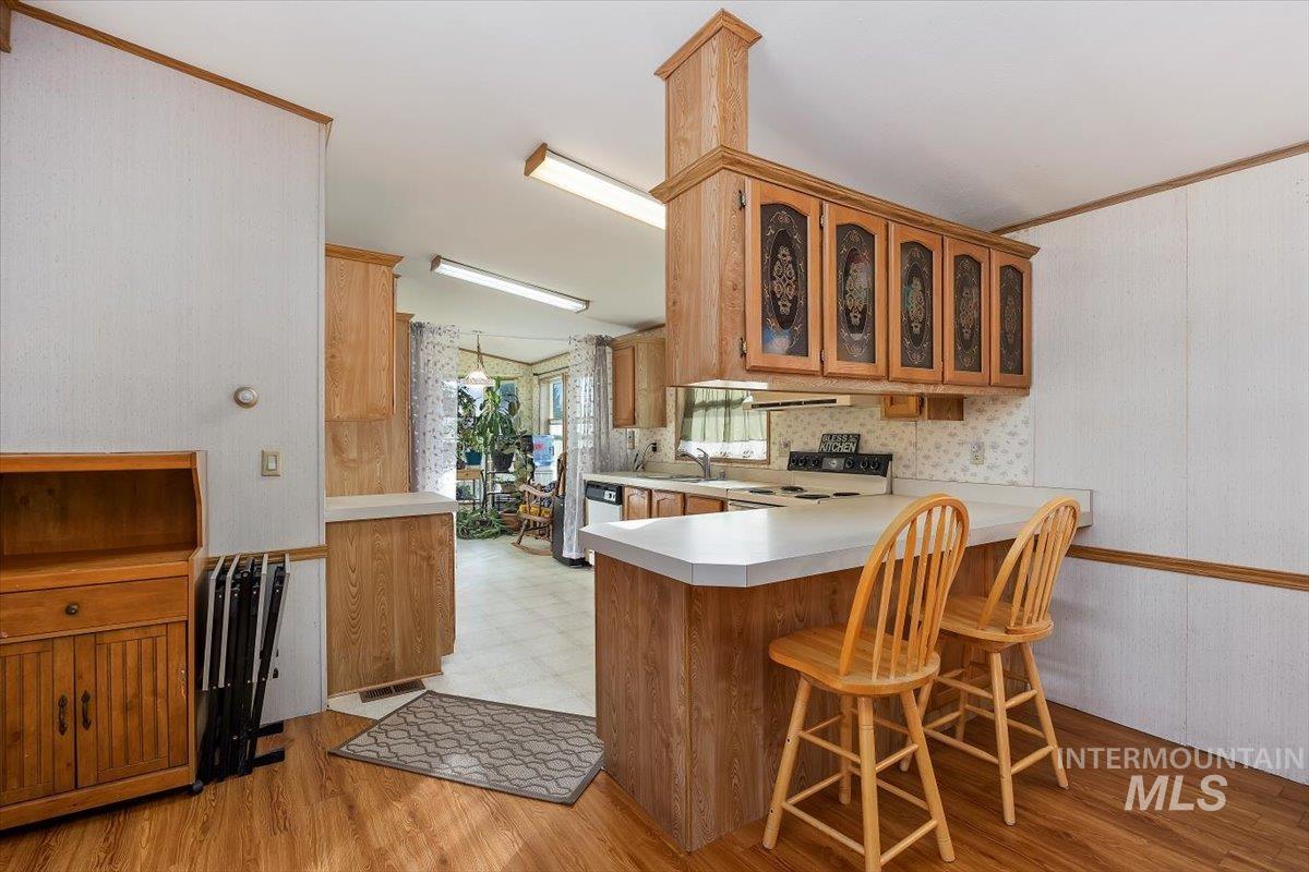 Kitchen featuring a peninsula, a kitchen breakfast bar, glass insert cabinets, light countertops, and light wood finished floors