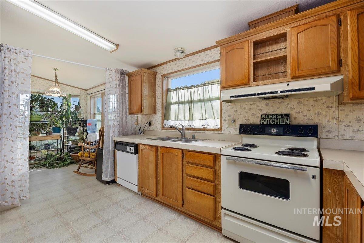Kitchen featuring wallpapered walls, white appliances, light flooring, light countertops, and brown cabinetry
