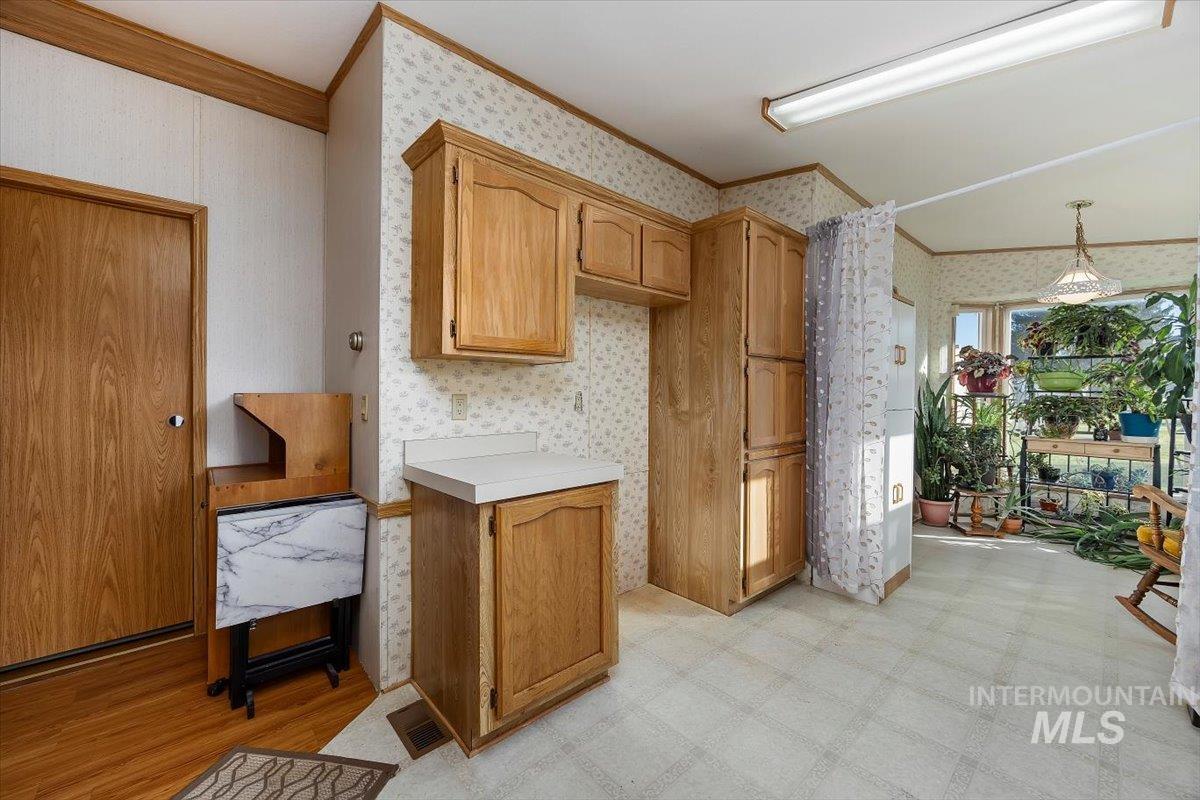 Kitchen featuring light countertops, ornamental molding, light flooring, wallpapered walls, and brown cabinets