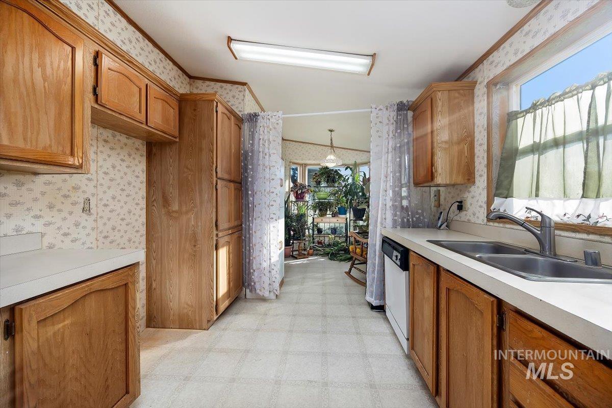 Kitchen with light floors, brown cabinets, light countertops, wallpapered walls, and decorative light fixtures