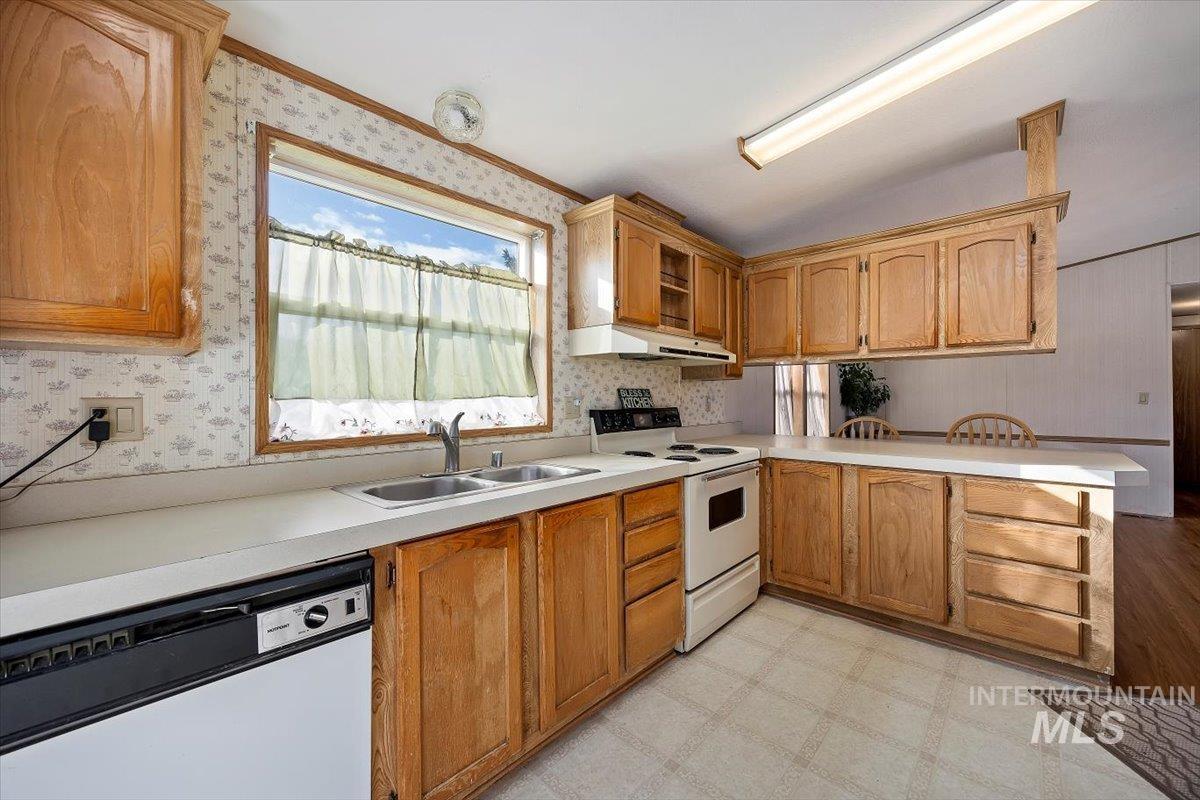 Kitchen featuring a peninsula, white appliances, light flooring, light countertops, and under cabinet range hood