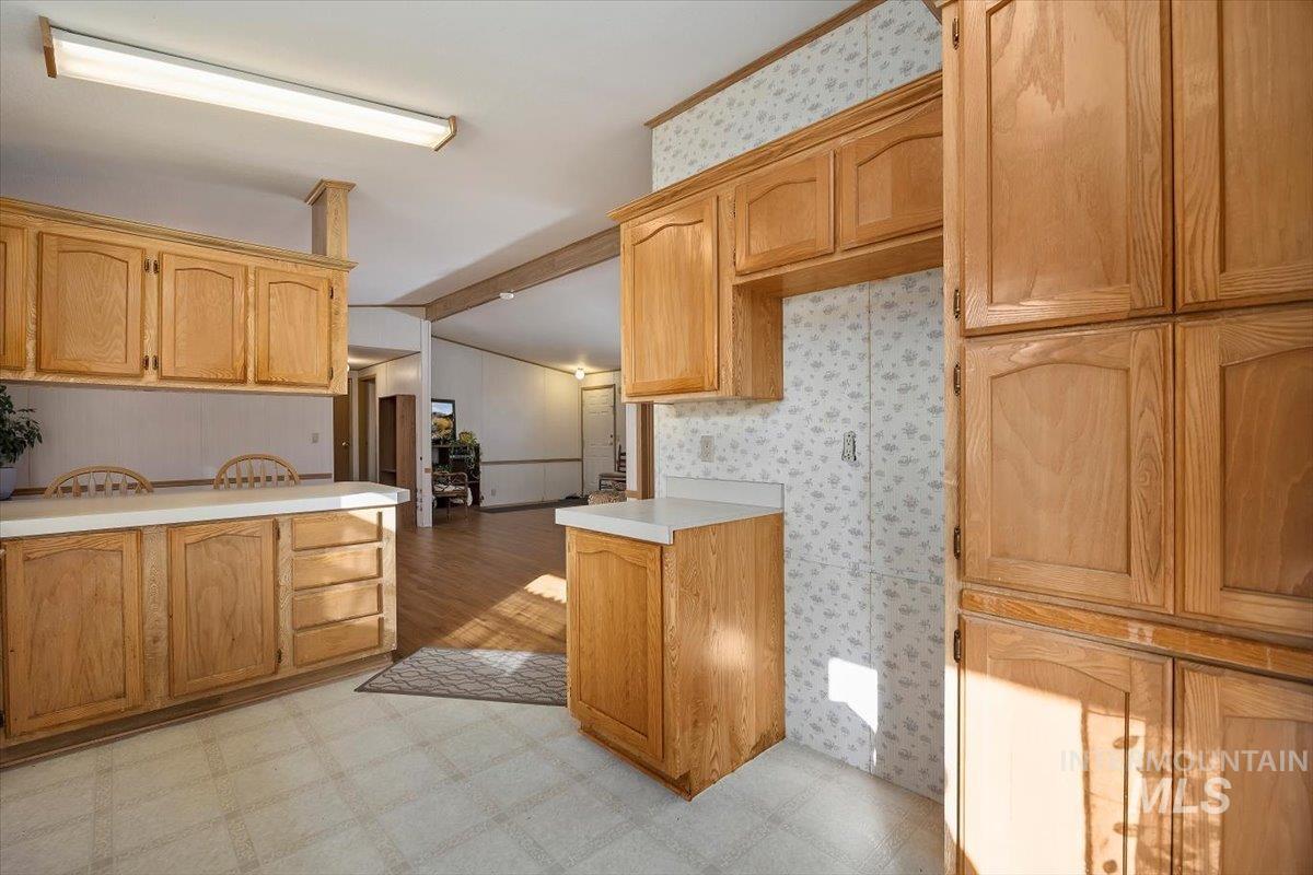 Kitchen featuring light flooring, light countertops, light brown cabinets, and wallpapered walls