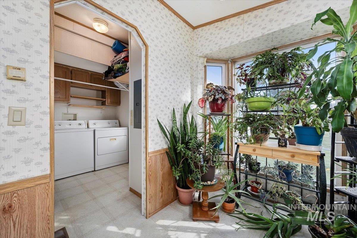 Laundry room with wainscoting, wallpapered walls, wood walls, washing machine and clothes dryer, and ornamental molding