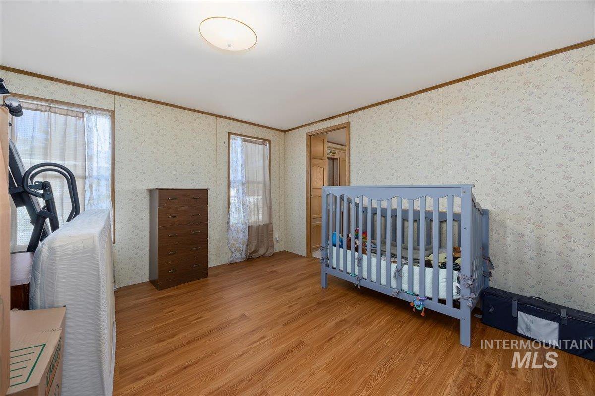 Bedroom with ornamental molding, wood finished floors, wallpapered walls, and a nursery area