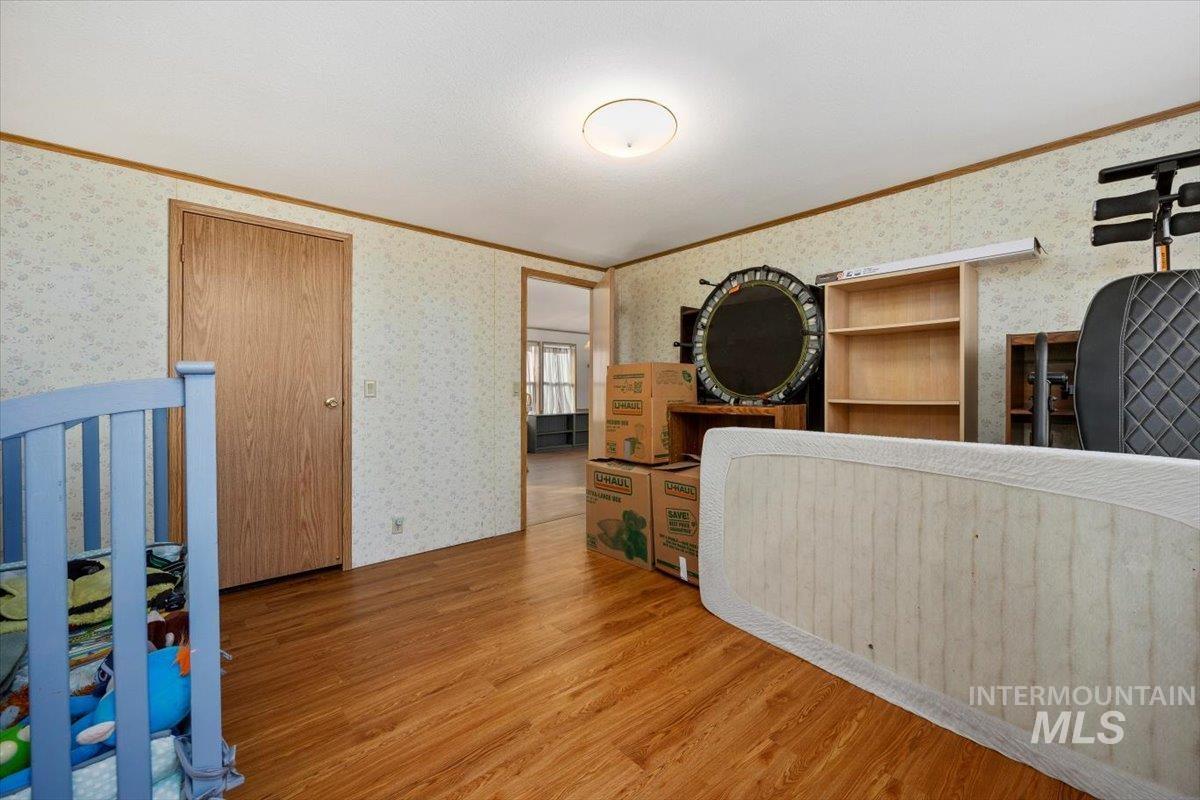 Interior space with ornamental molding, wallpapered walls, and wood finished floors