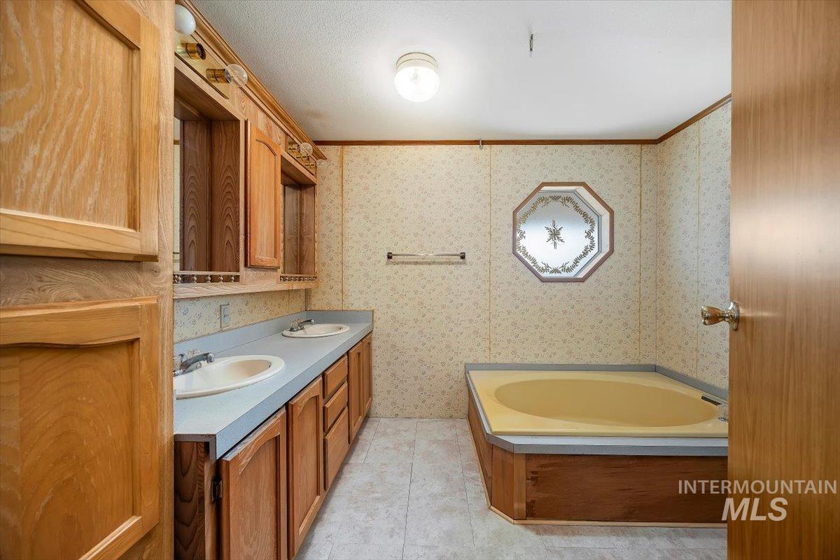 Bathroom featuring double vanity, a garden tub, ornamental molding, and wallpapered walls