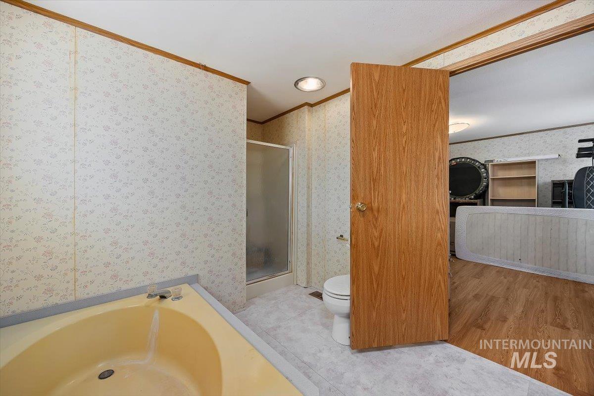 Full bath featuring a stall shower, a garden tub, ornamental molding, and light wood-style flooring