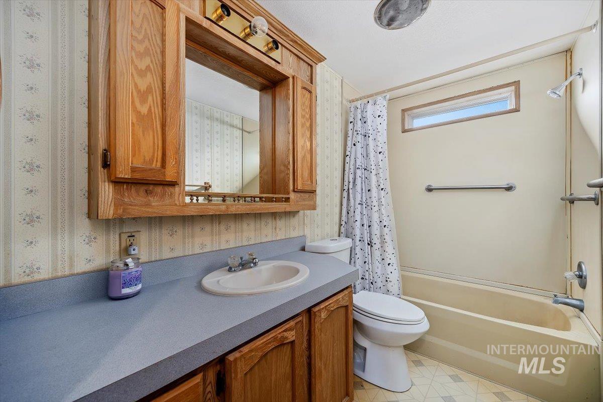 Full bathroom with vanity, shower / bath combo with shower curtain, and wallpapered walls