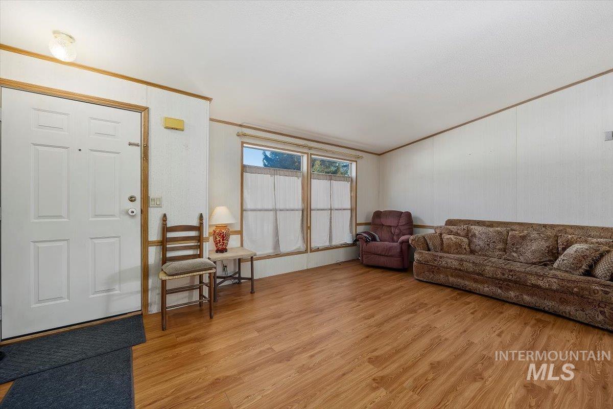 Living area featuring light wood-style flooring, ornamental molding, and vaulted ceiling