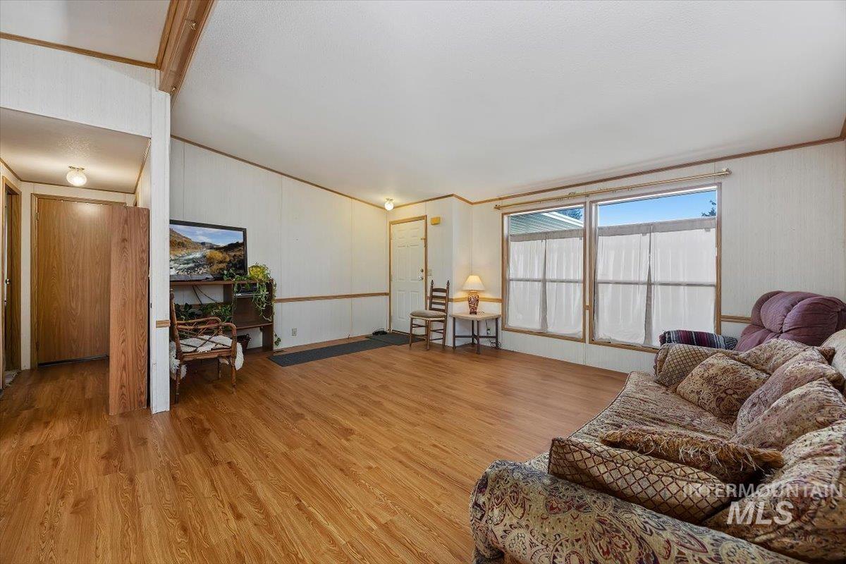 Living room with light wood finished floors, ornamental molding, and vaulted ceiling