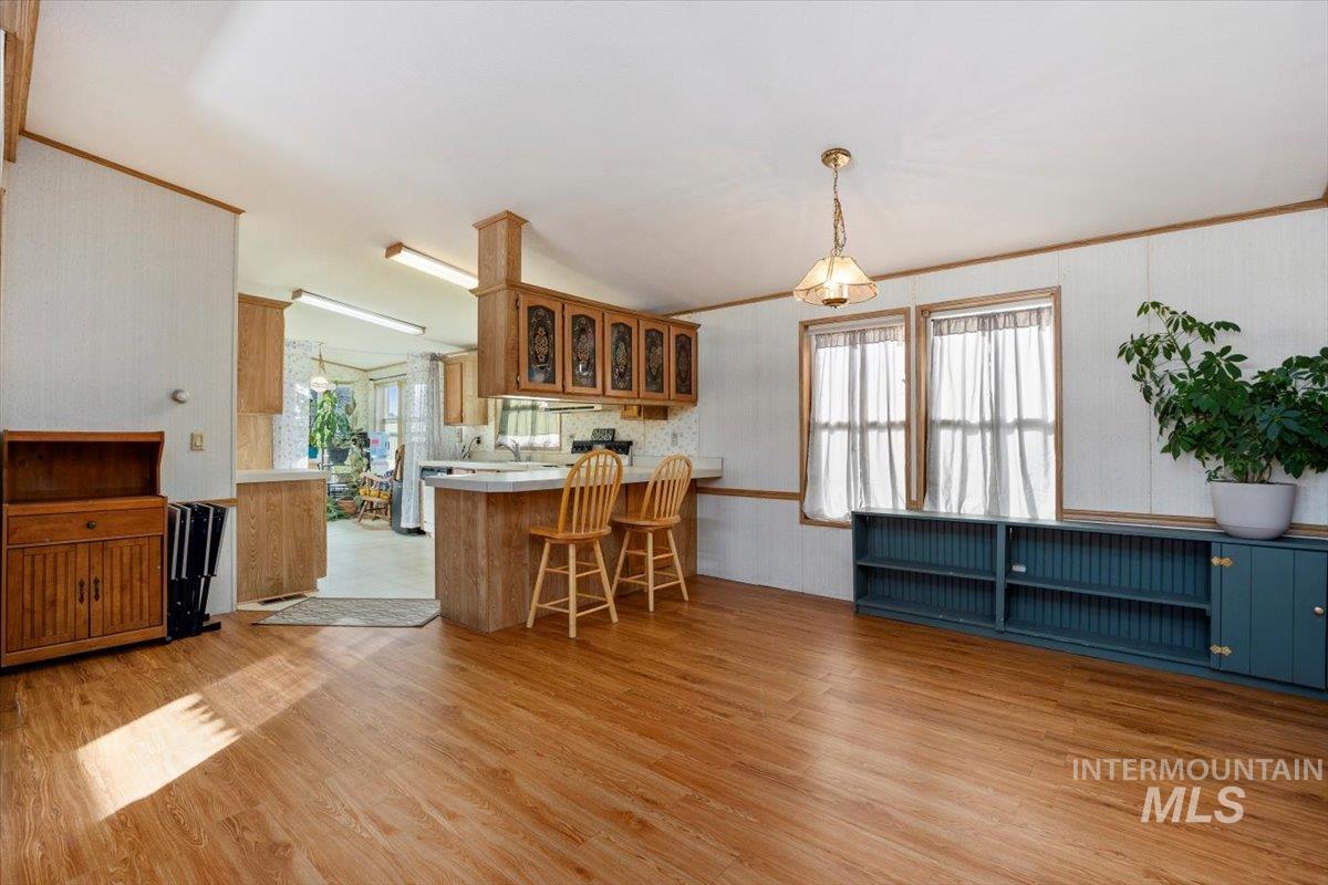 Kitchen with glass insert cabinets, a breakfast bar, light wood finished floors, a peninsula, and pendant lighting