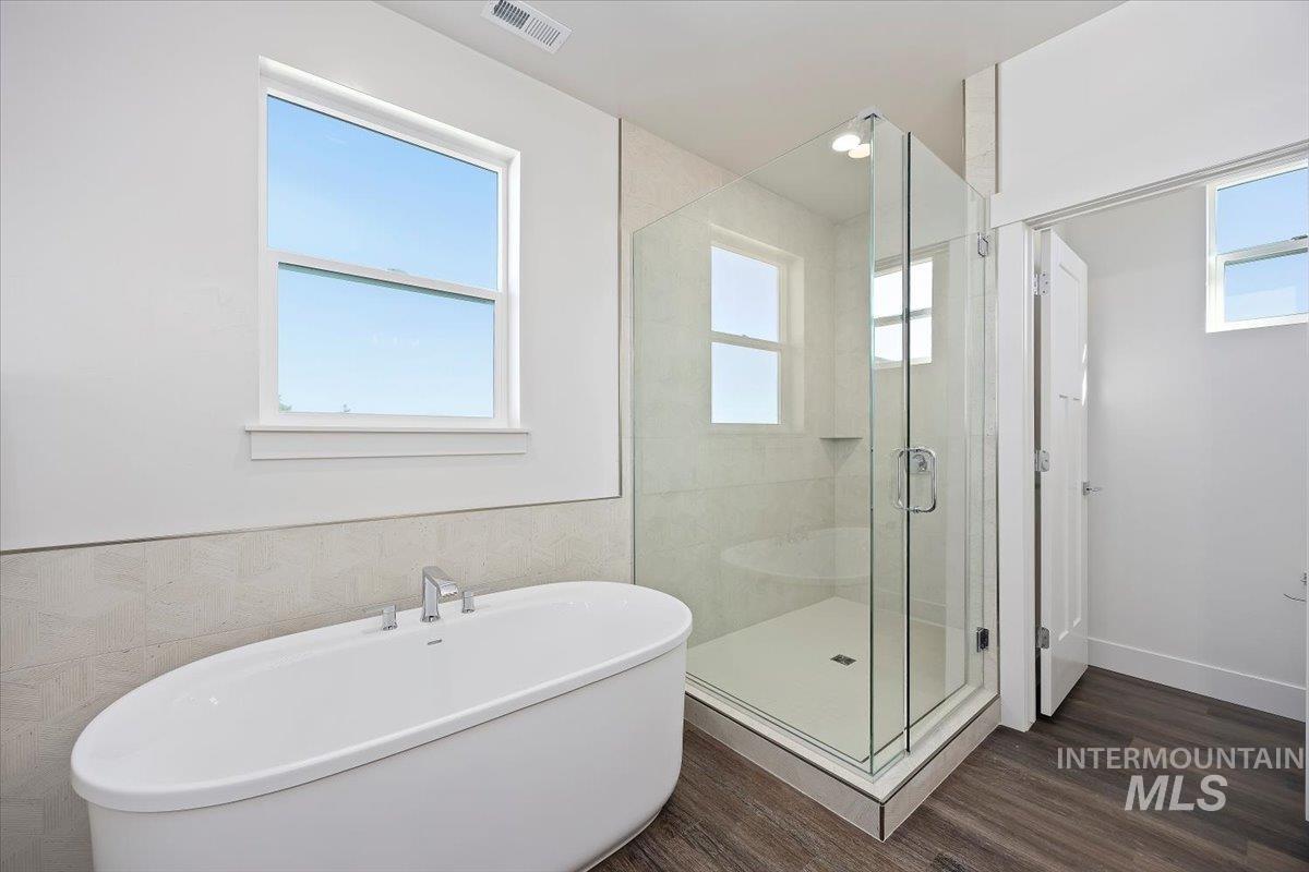 Bathroom with a freestanding bath, dark wood finished floors, a shower stall, and tile walls