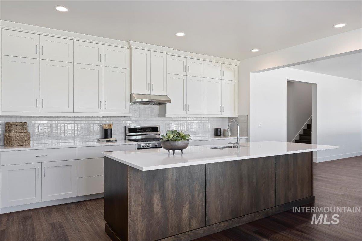 Kitchen featuring white cabinets, dark wood finished floors, decorative backsplash, recessed lighting, and a center island with sink