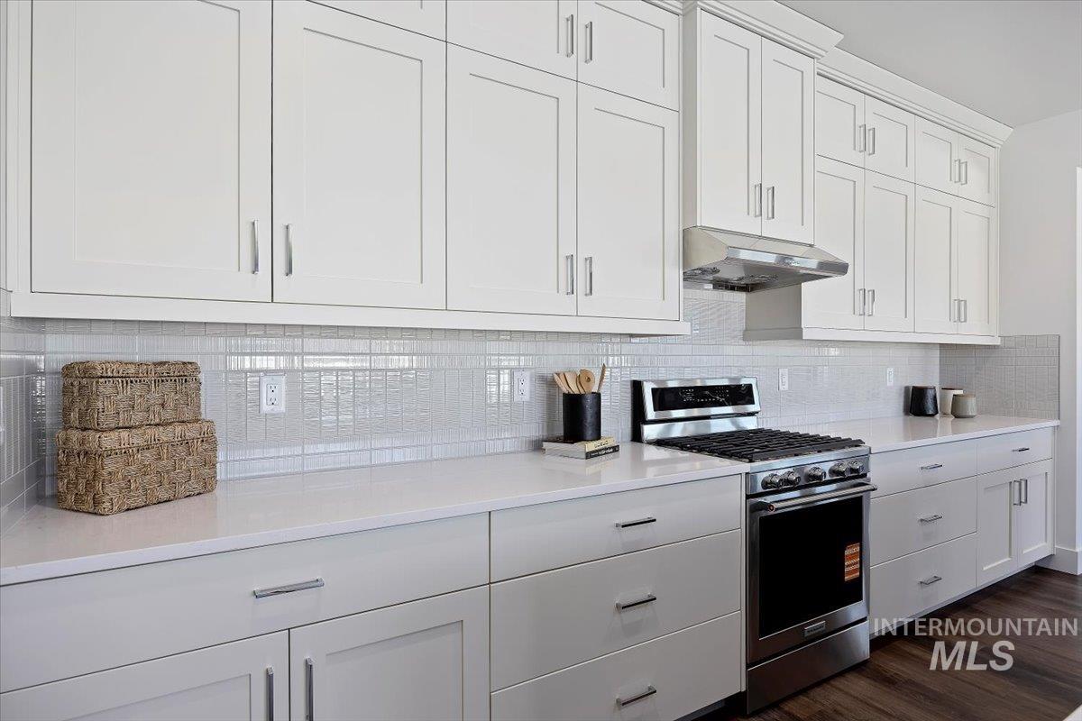 Kitchen with stainless steel range with gas cooktop, white cabinets, tasteful backsplash, and under cabinet range hood