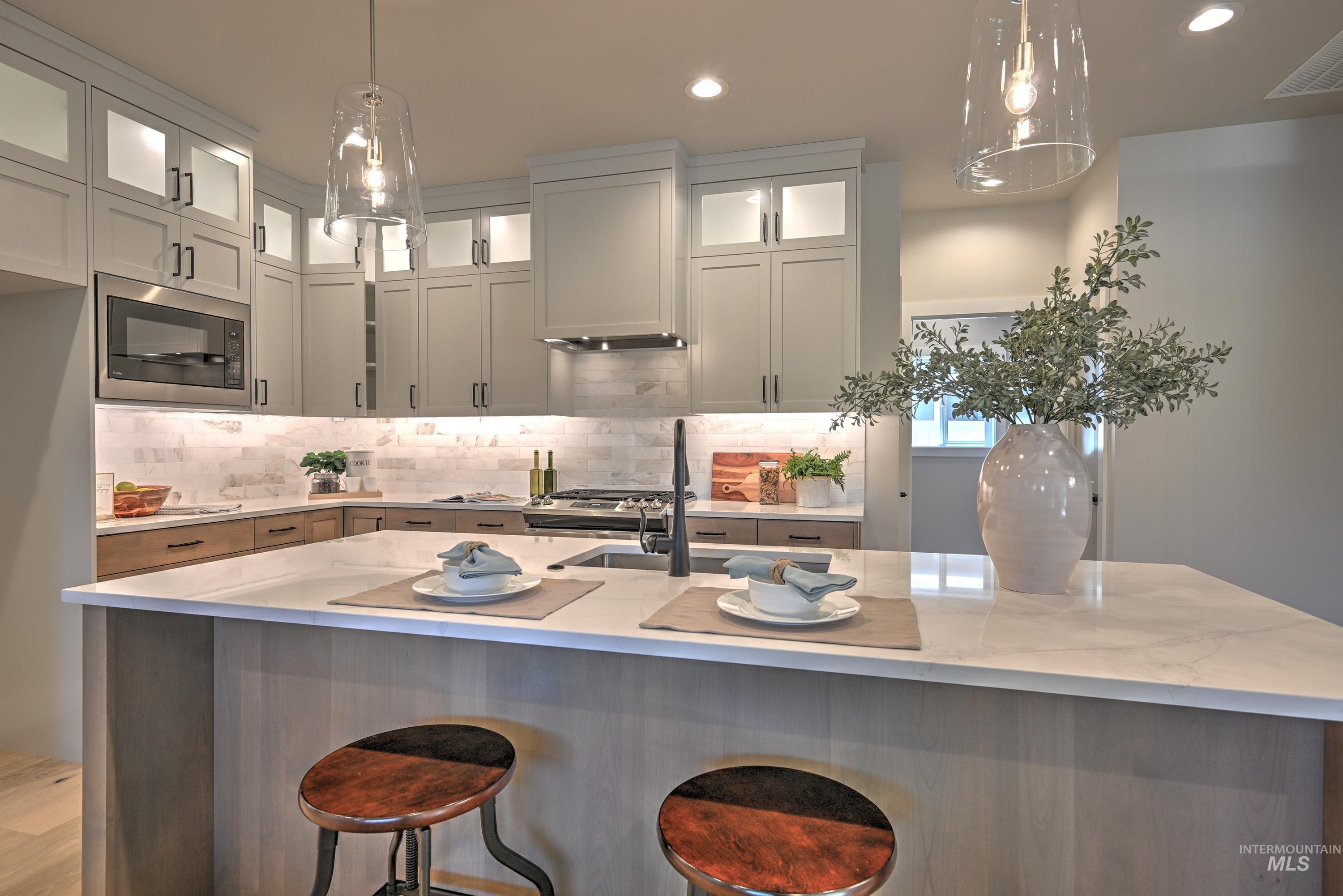Kitchen with black microwave, light stone counters, decorative backsplash, recessed lighting, and pendant lighting
