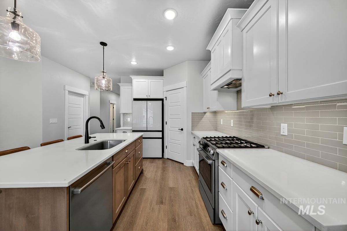 Kitchen with stainless steel appliances, white cabinetry, dark wood finished floors, decorative backsplash, and hanging light fixtures