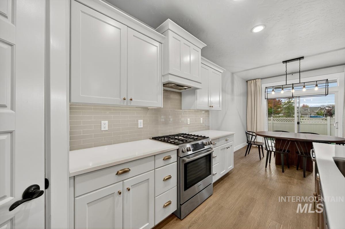Kitchen featuring stainless steel gas stove, light wood-type flooring, backsplash, white cabinets, and recessed lighting