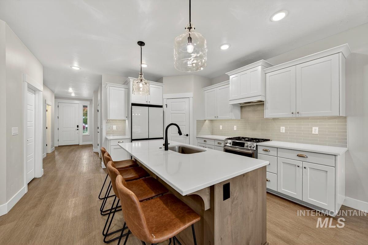 Kitchen featuring white cabinetry, a kitchen island with sink, a breakfast bar area, tasteful backsplash, and recessed lighting