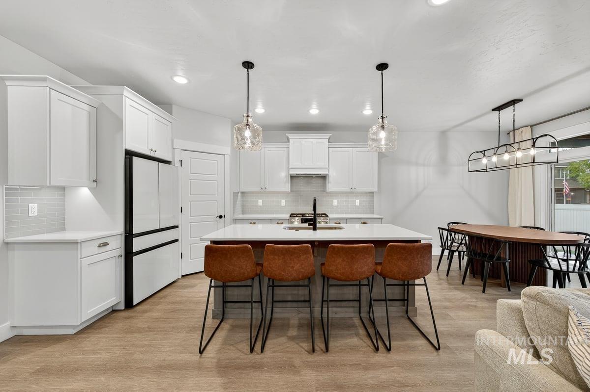 Kitchen featuring a breakfast bar area, pendant lighting, backsplash, an island with sink, and light wood-style flooring