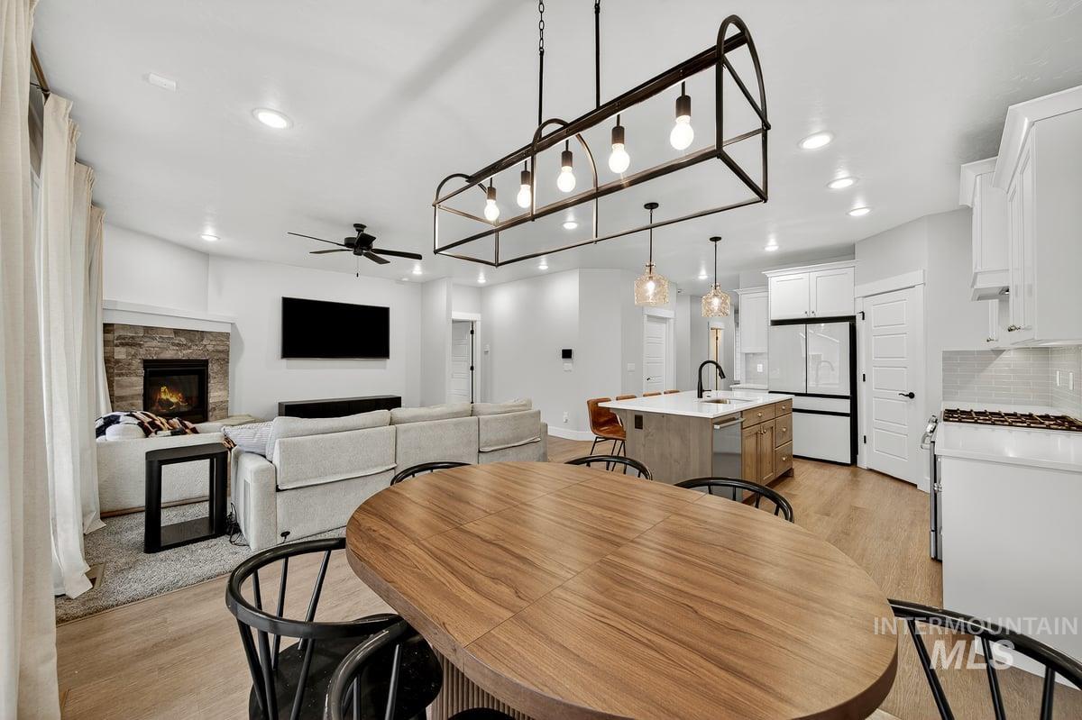 Dining room with light wood-style flooring, a ceiling fan, a stone fireplace, and recessed lighting