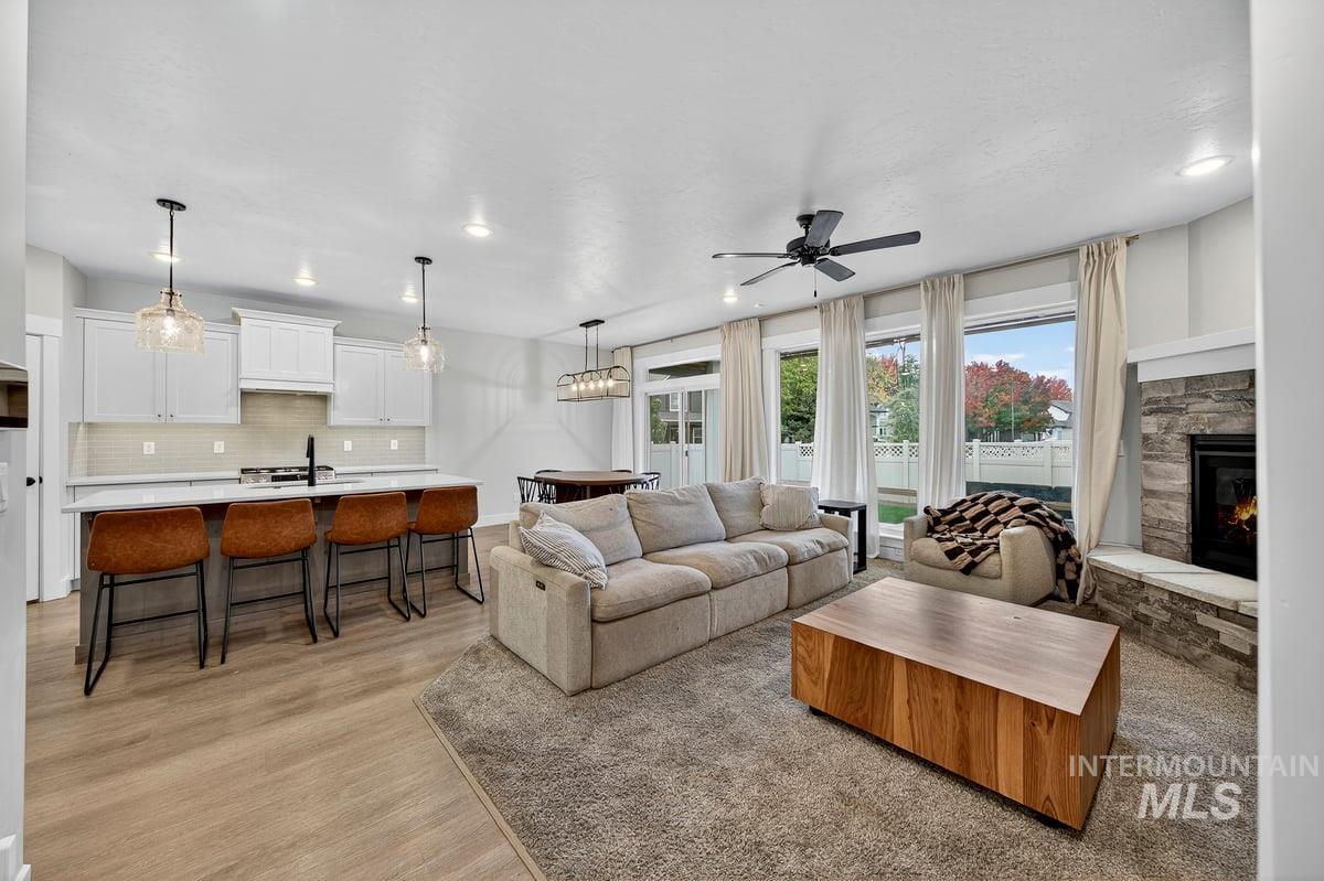 Living area featuring a ceiling fan, a stone fireplace, light wood finished floors, and recessed lighting