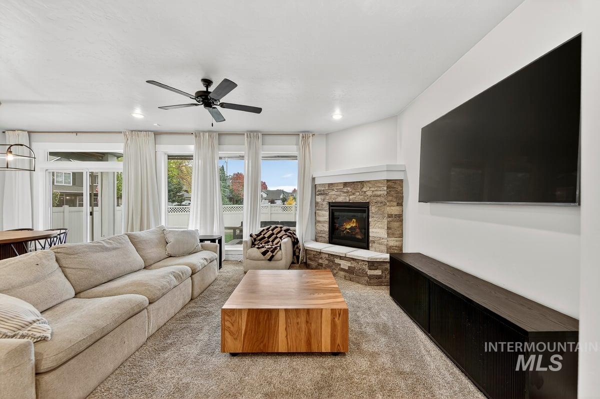 Living area with light colored carpet, a stone fireplace, and ceiling fan