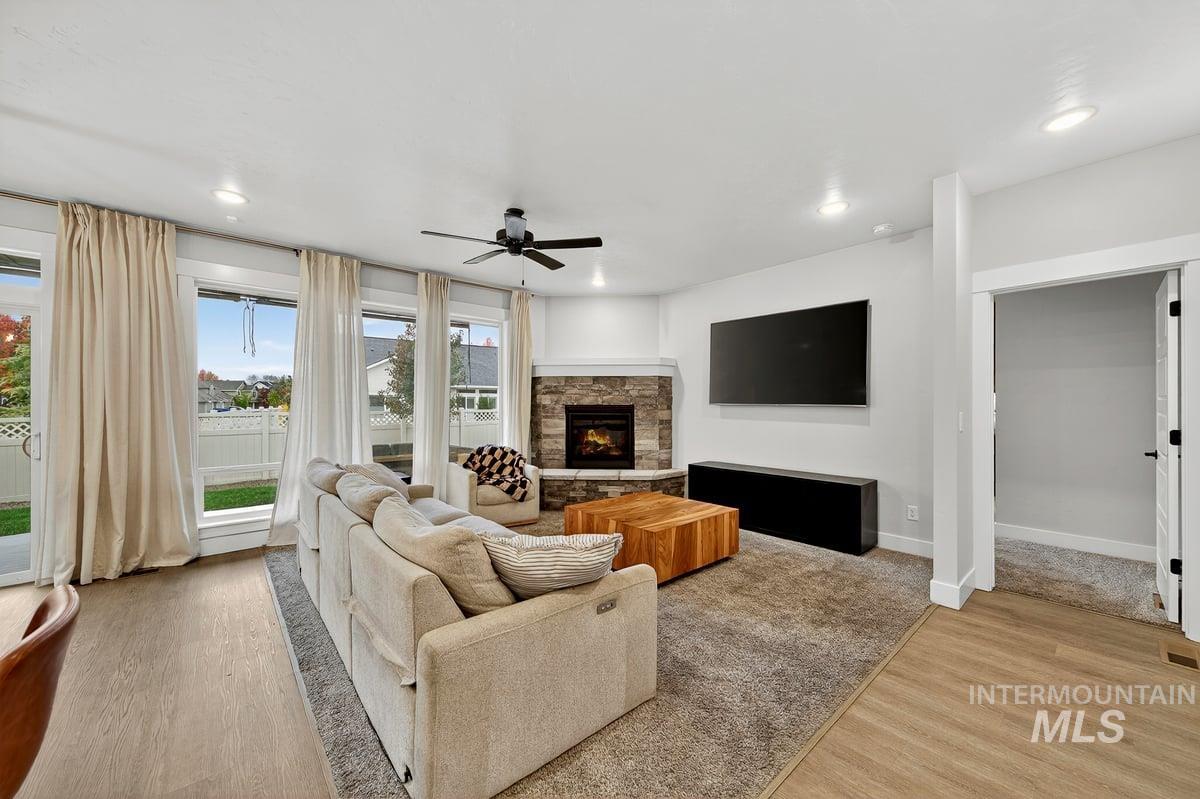Living room featuring light wood-style floors, a stone fireplace, a ceiling fan, and recessed lighting