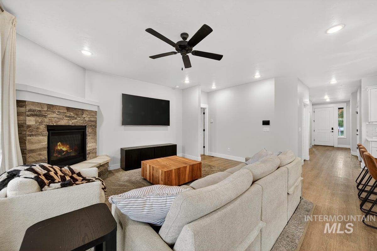 Living area with light wood finished floors, a stone fireplace, ceiling fan, and recessed lighting