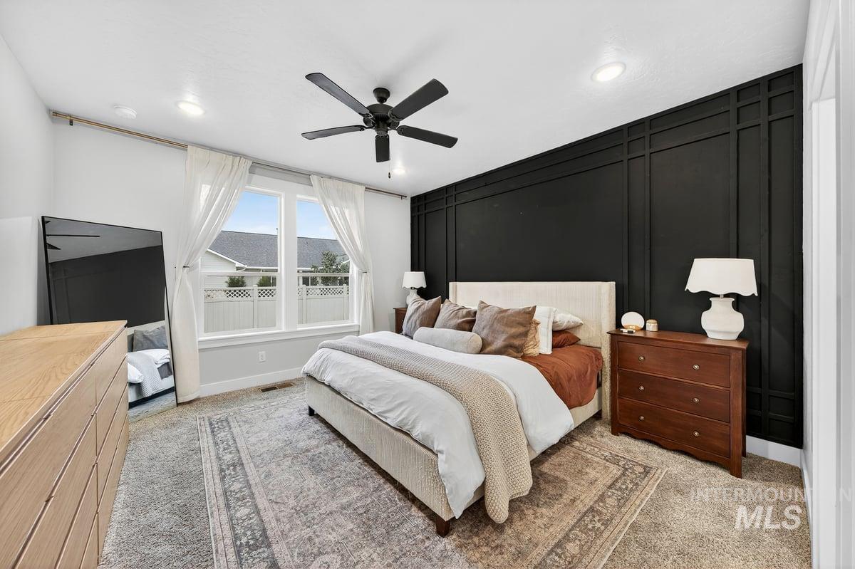 Bedroom with light colored carpet, a decorative wall, and a ceiling fan