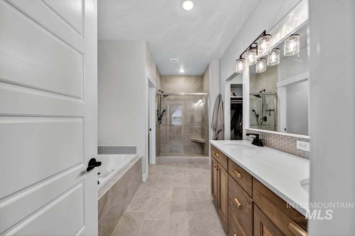 Bathroom featuring double vanity, a stall shower, a garden tub, recessed lighting, and backsplash